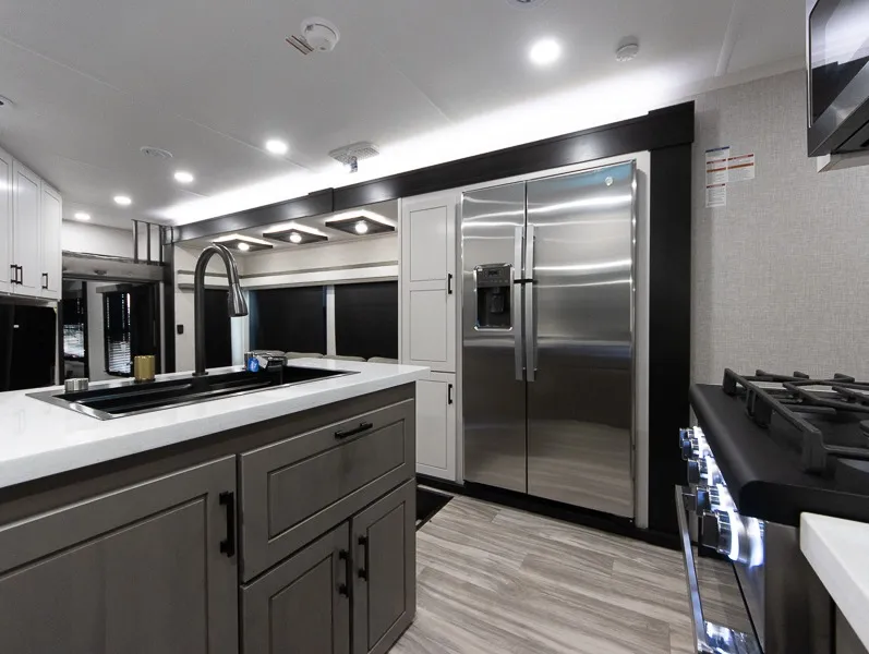 2025 Jayco Seismic Luxury Series 4113 — Kitchen island sink, refrigerator, pantry cabinet, range, and surrounding countertops viewed across the cooking area