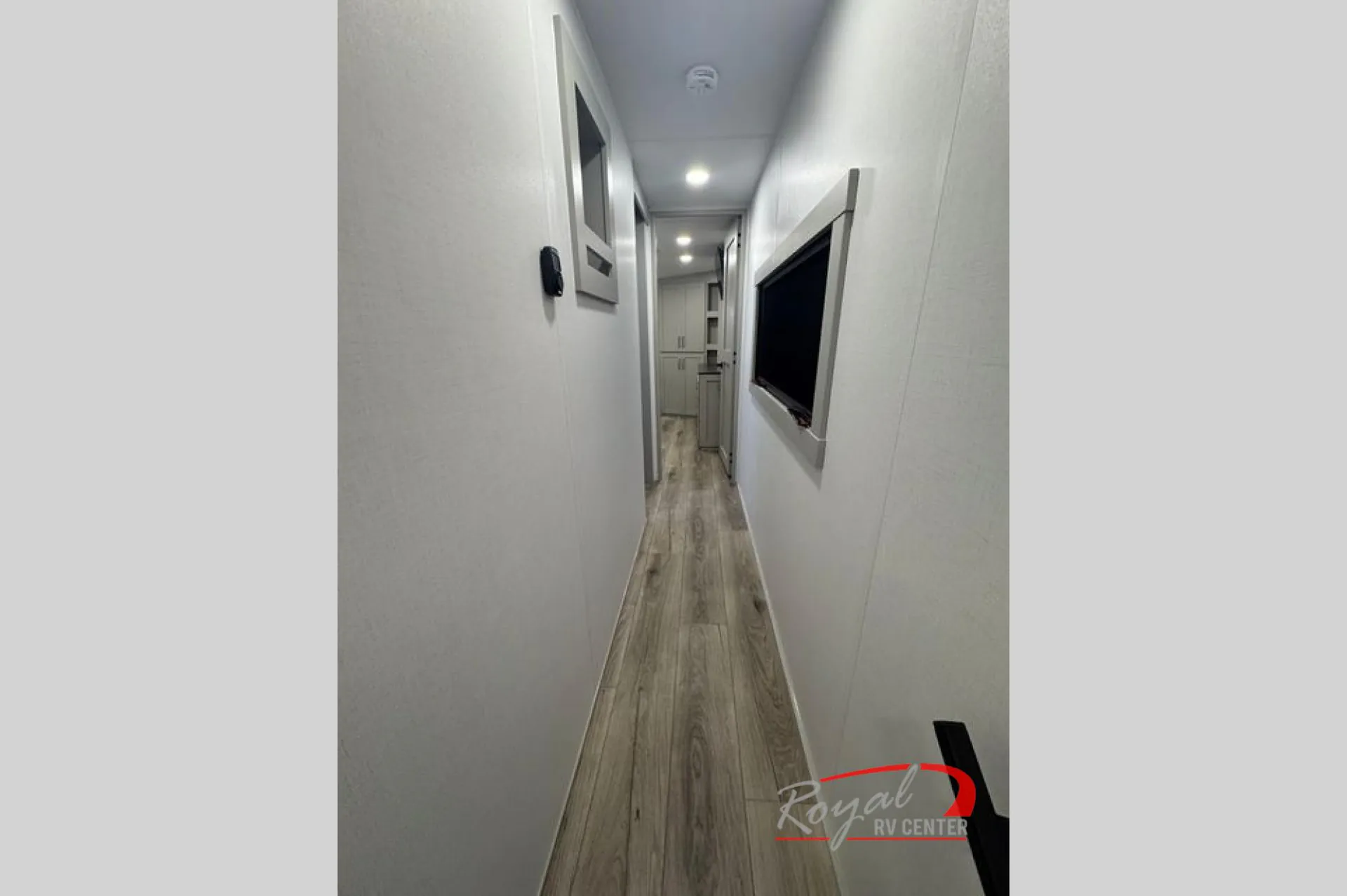 2026 Brinkley Model Z 3610 — Narrow fifth-wheel hallway with wood-look flooring, wall-mounted television, doors, and overhead lights