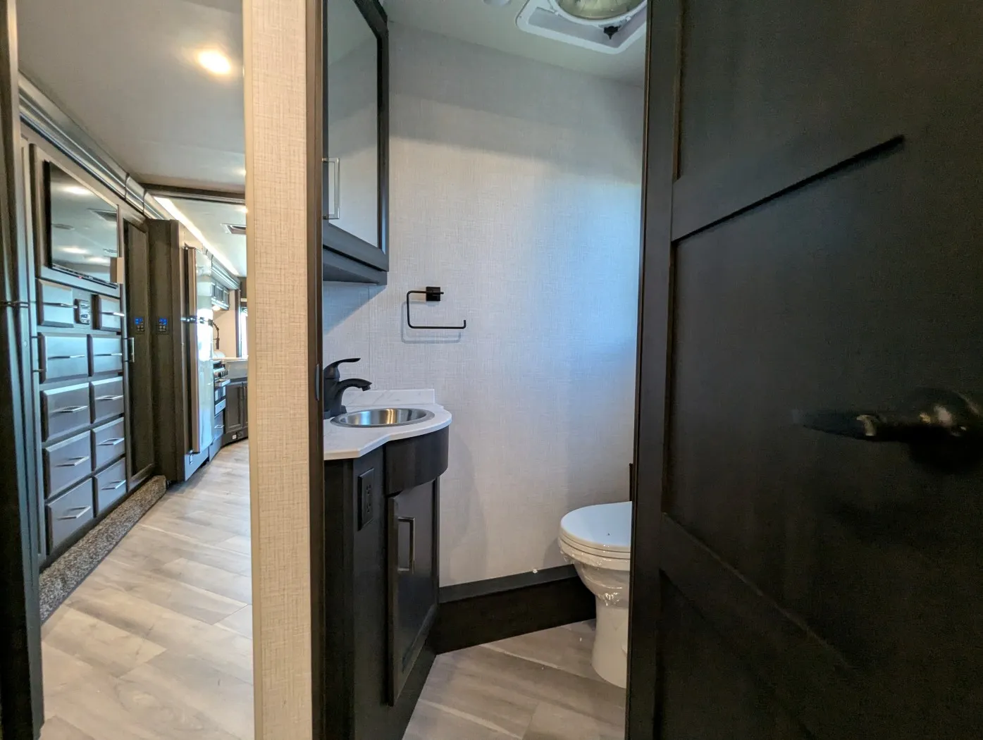 2026 Holiday Rambler Invicta 36Y — Open bathroom with a sink vanity, toilet, overhead cabinet, and roof vent beside the interior aisle