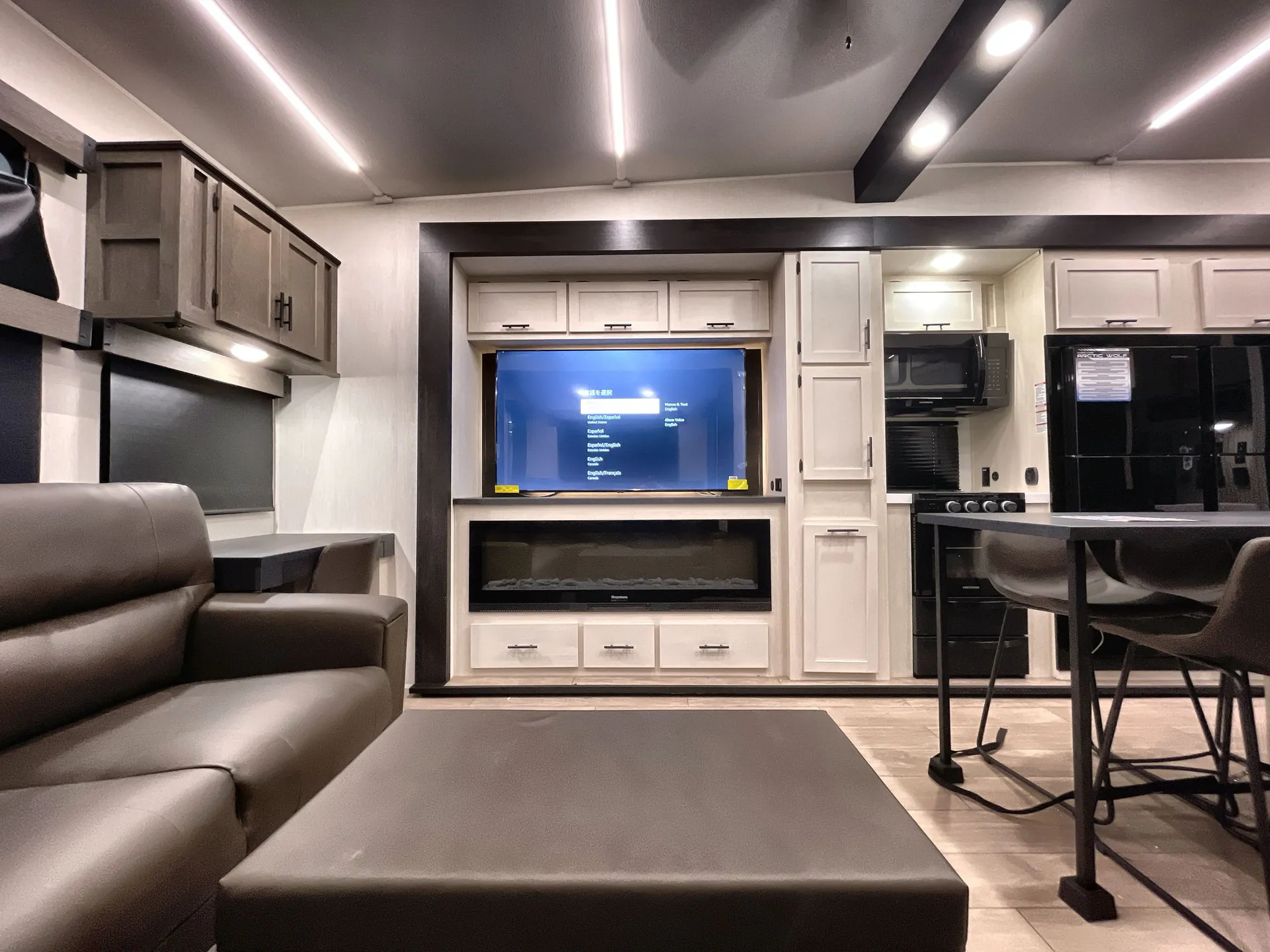 2026 Forest River Arctic Wolf 38LEAH.G — Living room with sofas, ottoman, entertainment center, adjacent kitchen appliances, and dining table