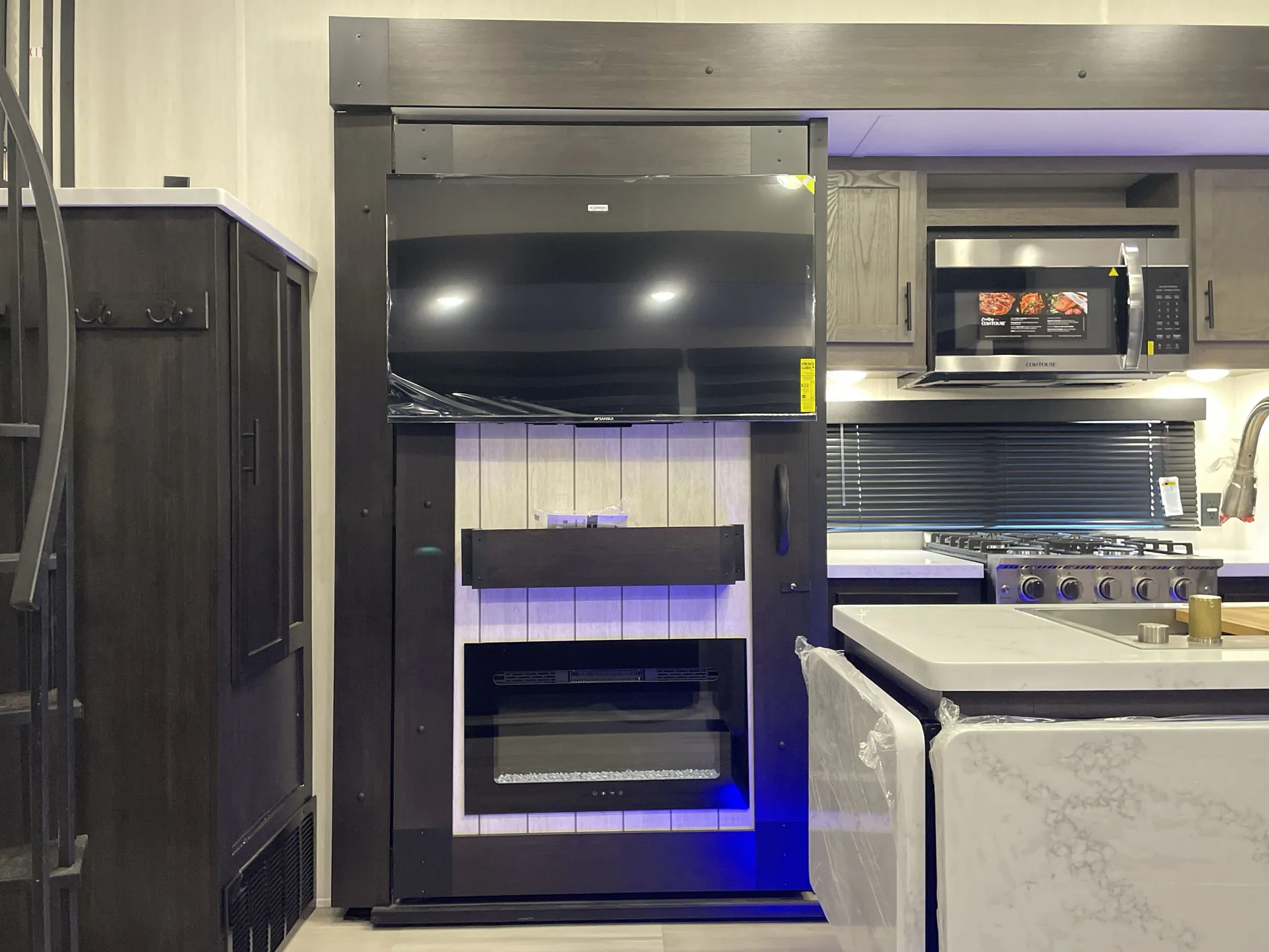 2026 Forest River Cherokee Wolf Pack 397STAY — Living entertainment wall with television and fireplace beside the kitchen island, microwave, and gas range
