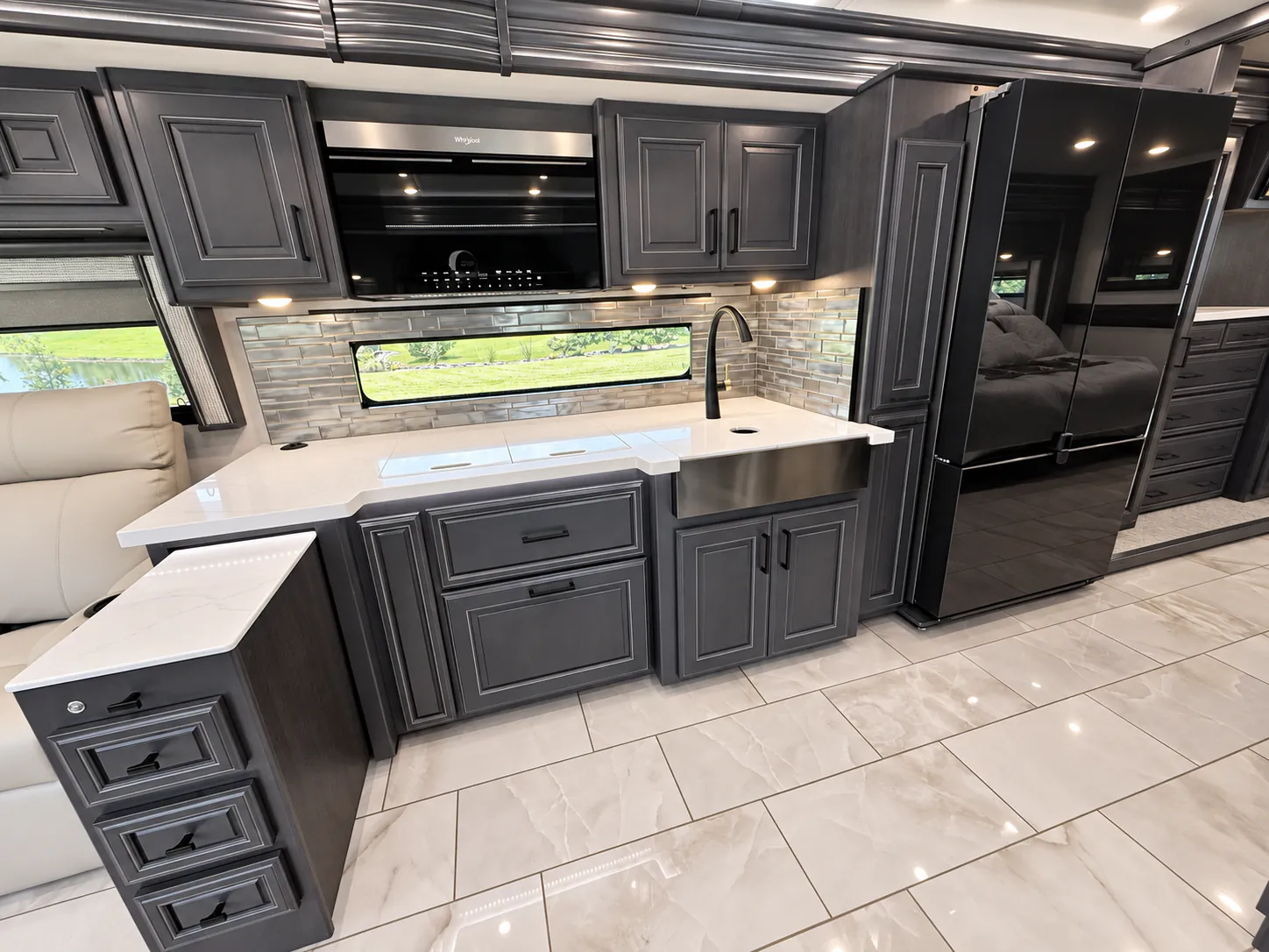 2027 Fleetwood Discovery LXE 40M — Class A motorhome kitchen with white countertop, sink, cooktop, oven, refrigerator, backsplash, and extensive dark cabinetry