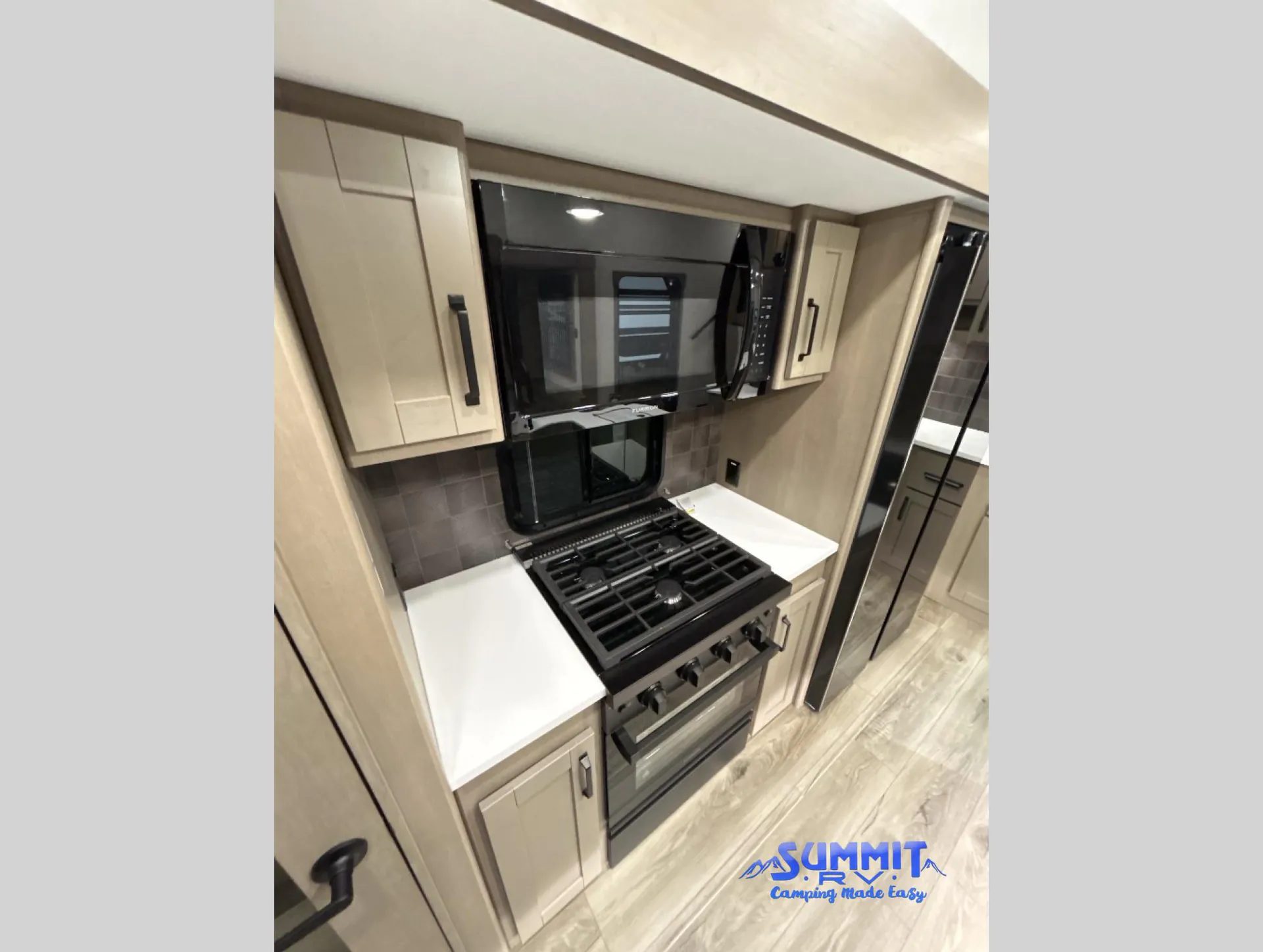 2027 Grand Design Reflection 362TBS — Kitchen range and oven beneath a microwave, flanked by countertops, cabinets, and a tall refrigerator