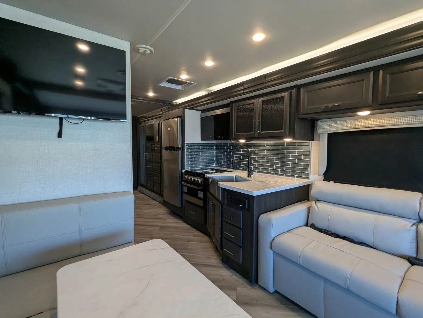 2026 Holiday Rambler Invicta 36Y — Kitchen with refrigerator, cooktop, sink, and cabinetry framed between a sofa and dinette table