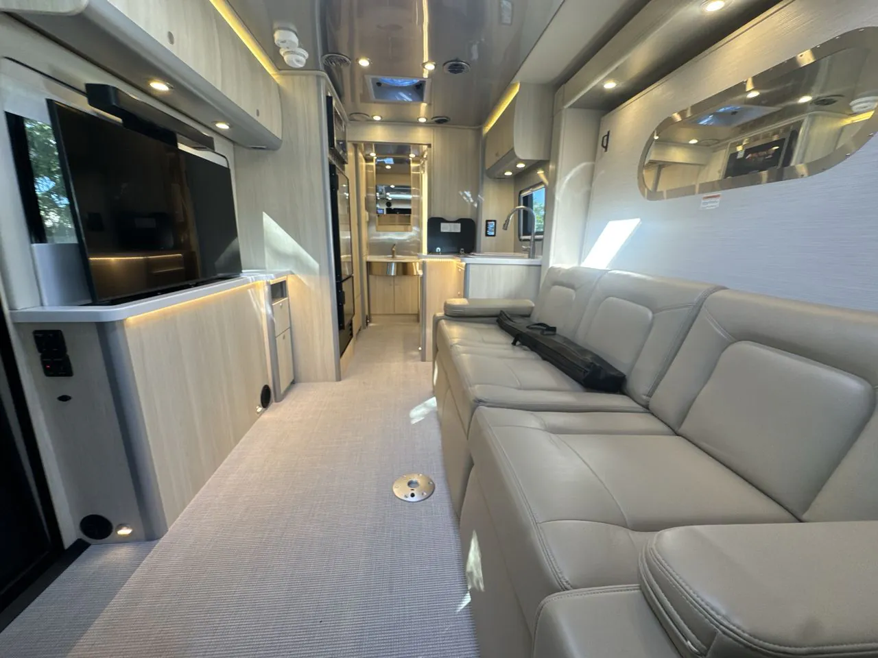 2026 Airstream Atlas Murphy Suite — Class B van lounge with leather sofa, television, and galley kitchen extending along the opposite side