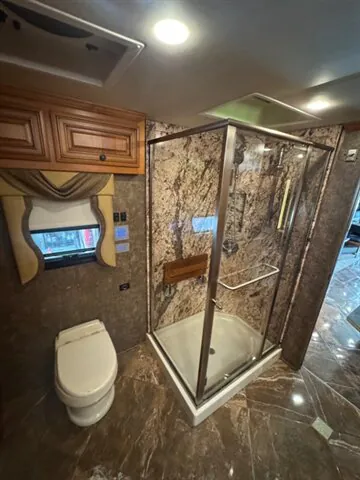 2016 Newmar Dutch Star 4369 — Bathroom with enclosed glass shower, toilet, vanity-side cabinetry, patterned walls, and a curtained window