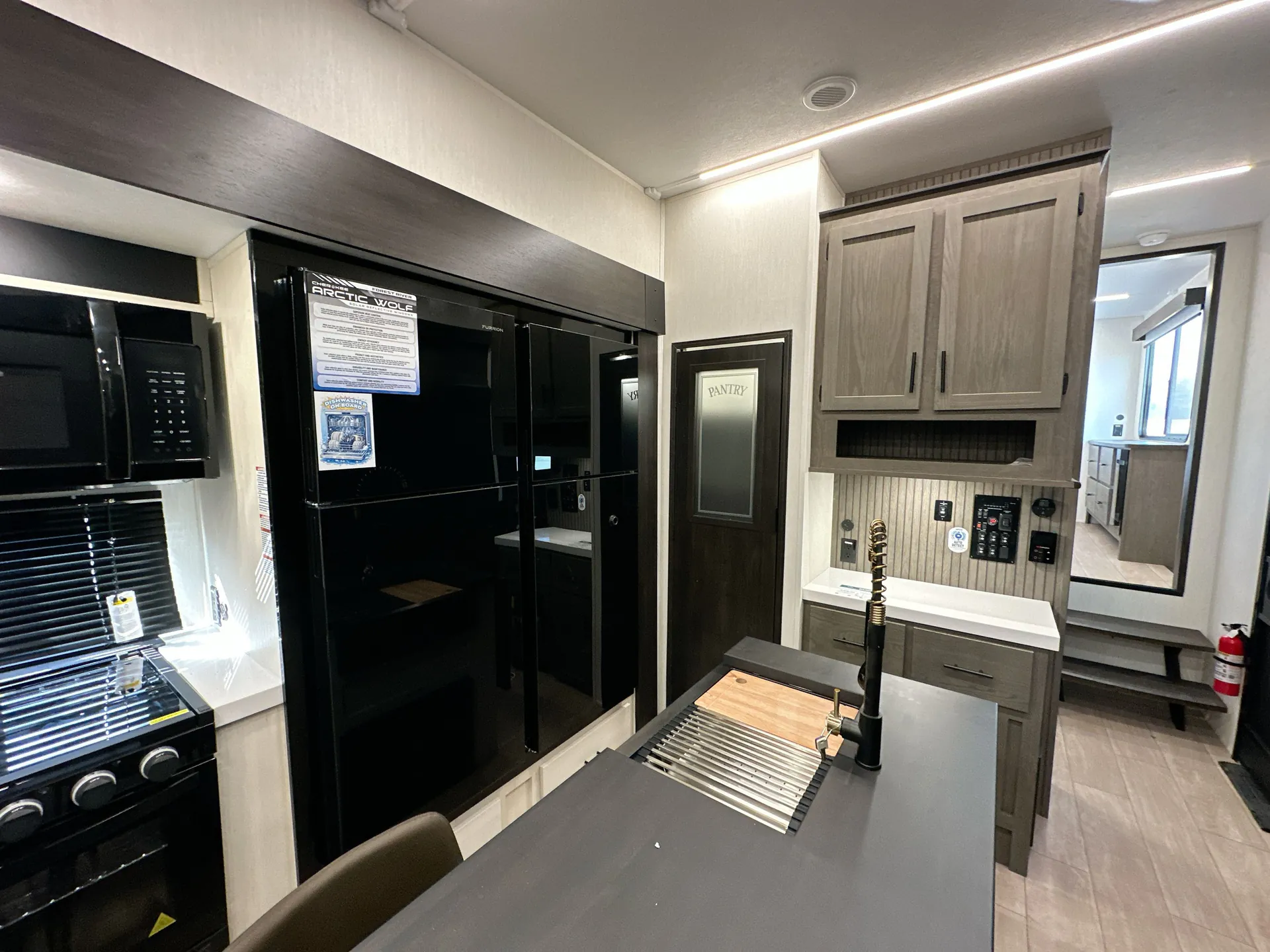 2026 Forest River Arctic Wolf 38LEAH.G — Fifth wheel kitchen with island sink, refrigerator, range, pantry, cabinets, and a hallway leading toward the rear