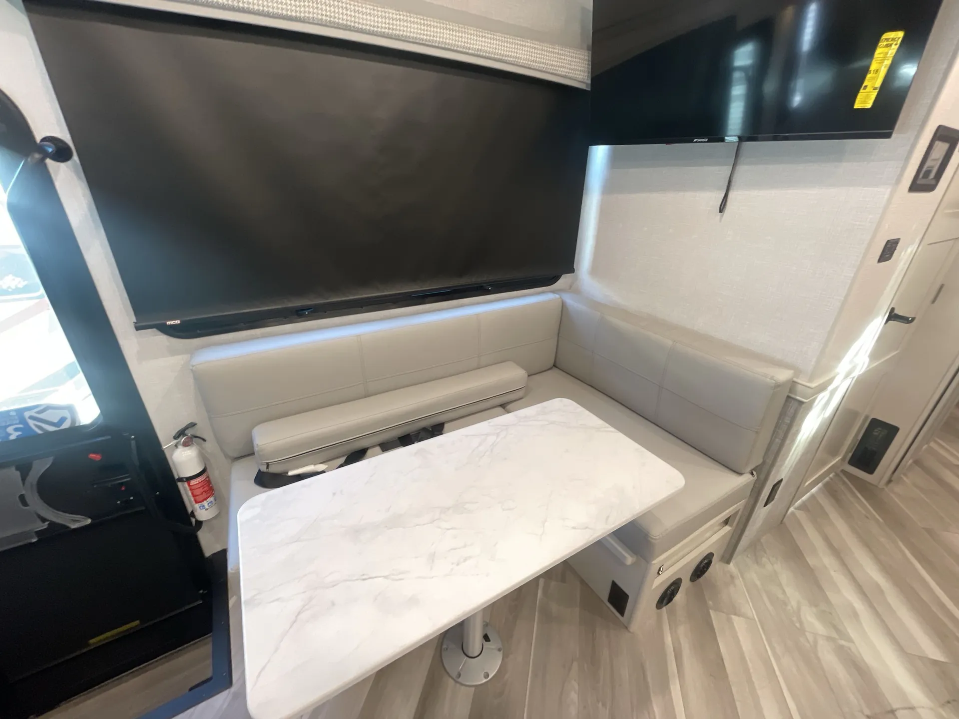 2026 Holiday Rambler Invicta 36Y — Dinette table and bench seating beneath televisions, with the cockpit visible beside the dining area