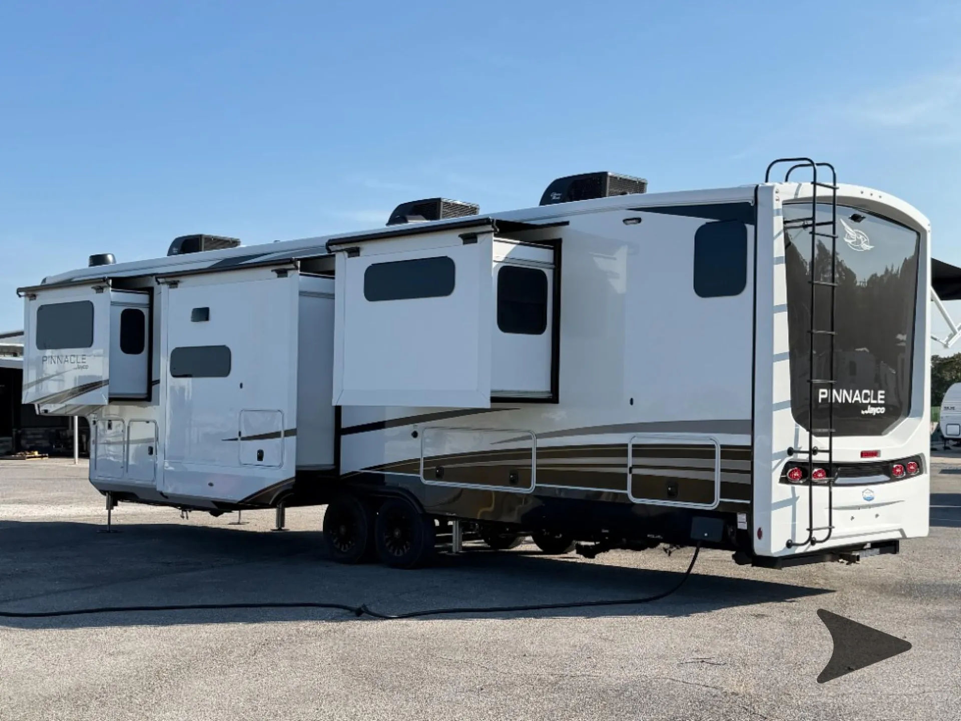 2027 Jayco Pinnacle 39FLOK — The outside rear and curb side of the fifth-wheel RV, including exterior walls, slide-outs, storage compartments, ladder, and wheels