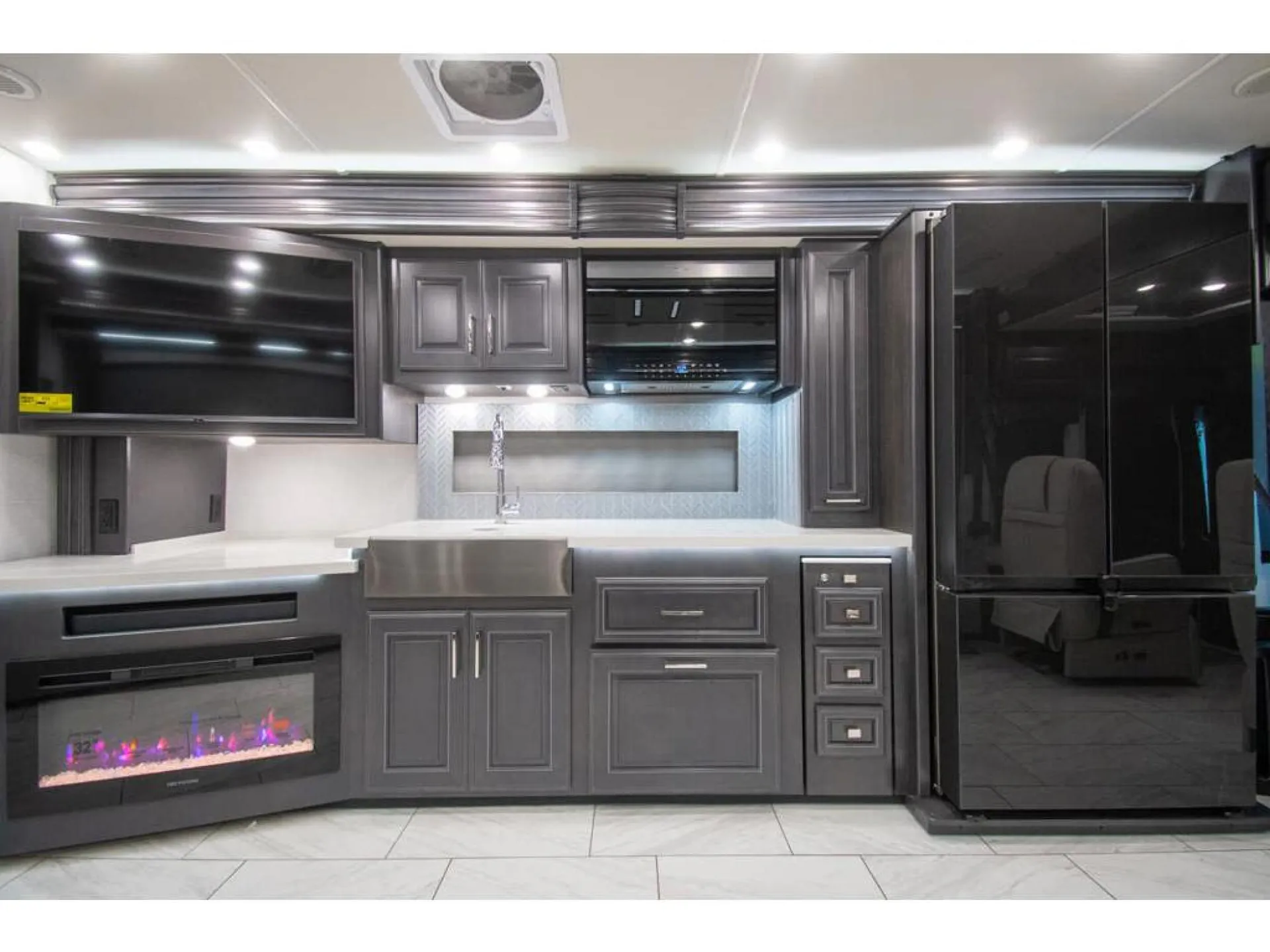 2026 Fleetwood Discovery LXE 40G — Class A kitchen wall with stainless sink, counter, cabinets, range hood, refrigerator and built-in fireplace