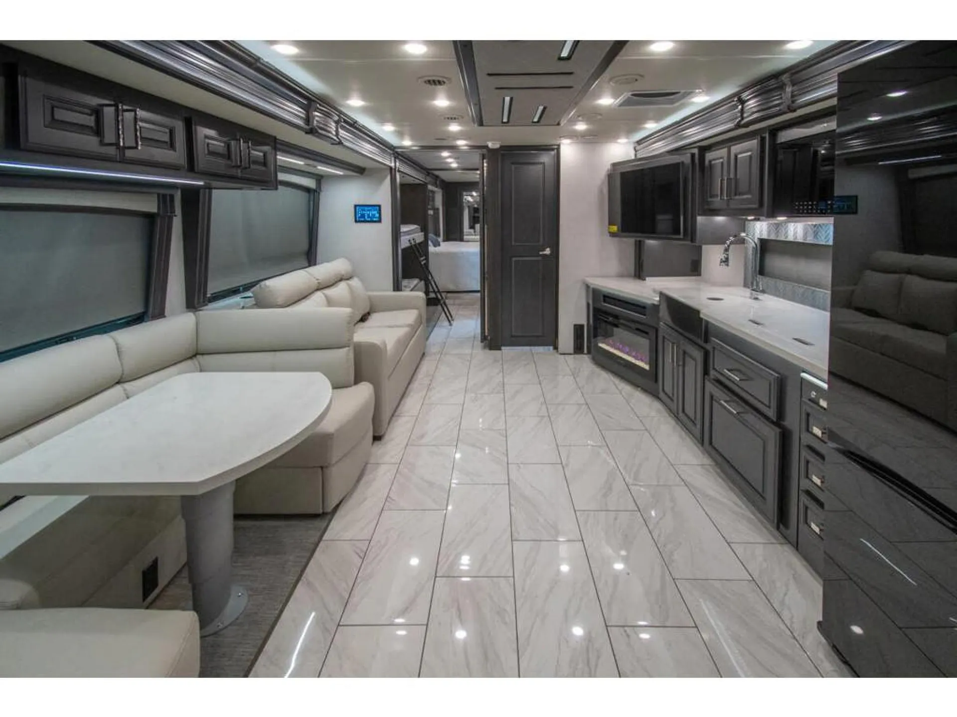 2026 Fleetwood Discovery LXE 40G — Motorhome interior overview with kitchen counters and appliances opposite lounge seating and a visible rear bed area