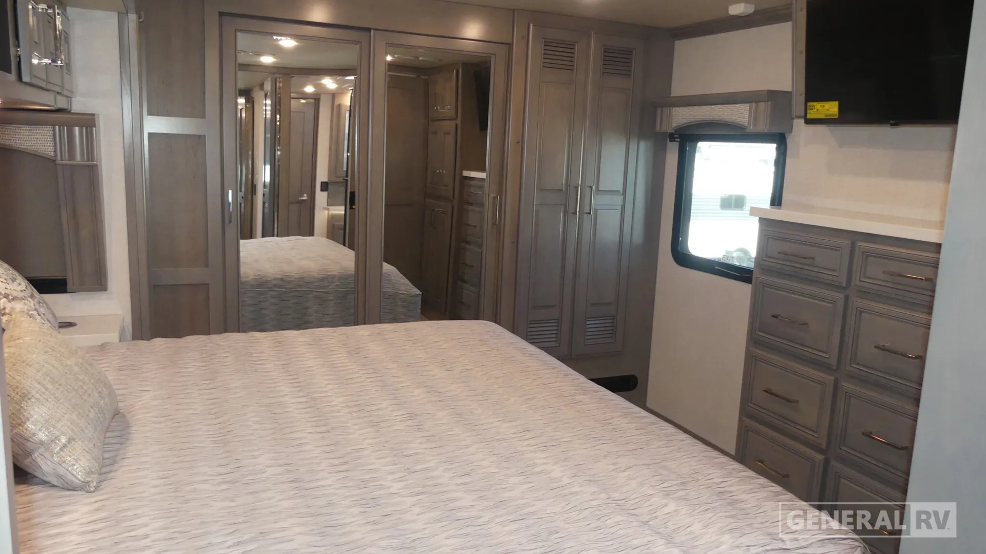 2026 Fleetwood Discovery LXE 40G — Main bedroom with bed, mirrored wardrobe doors, dresser, window, and wall-mounted television
