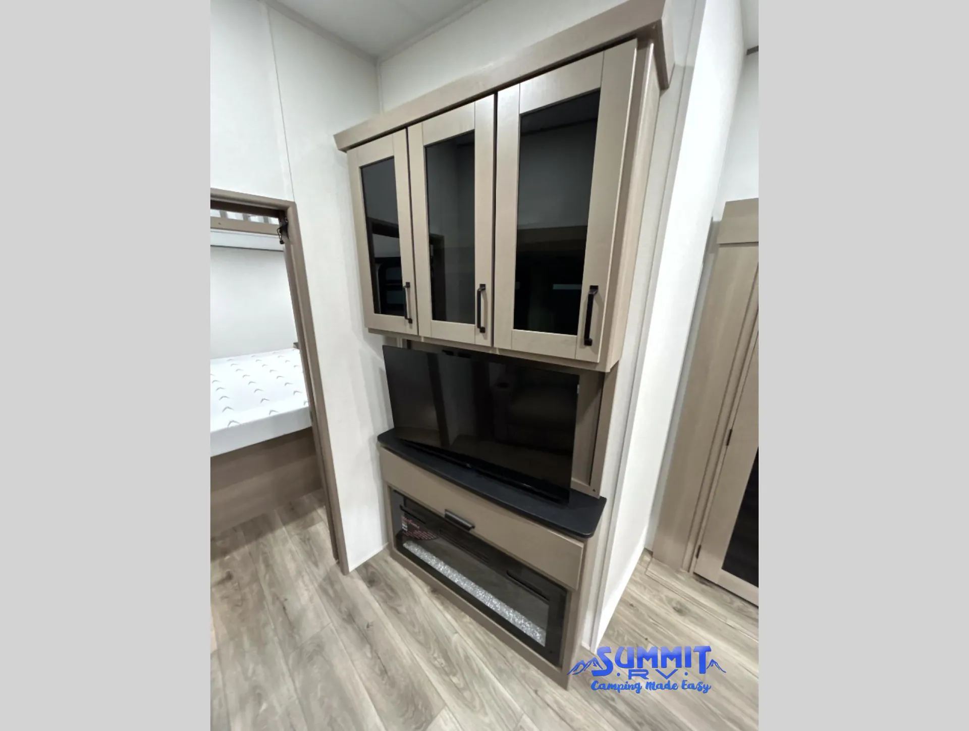 2027 Grand Design Reflection 362TBS — Entertainment center with television, glass-front cabinets, fireplace, and adjacent doorway to a bed