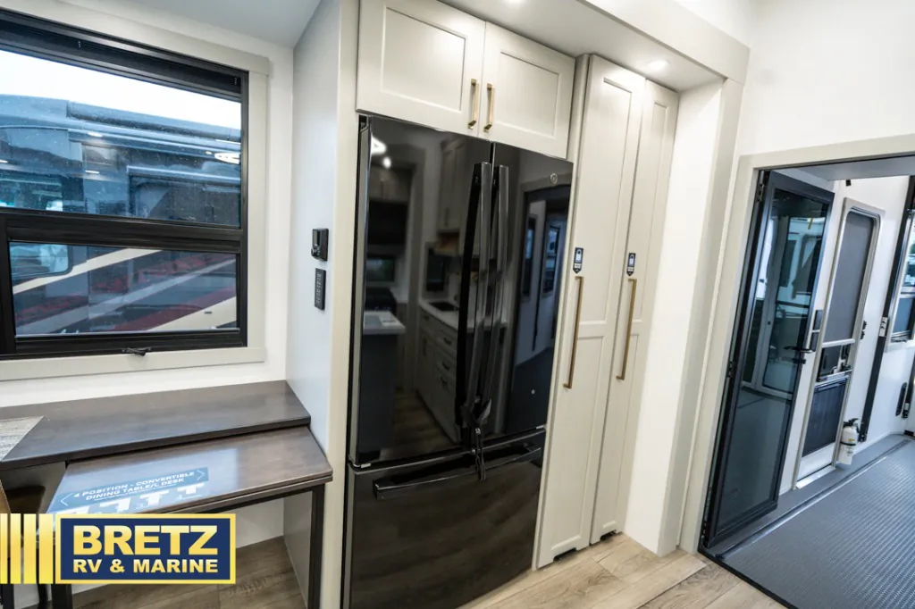 2026 Brinkley Model G 3950 — Fifth wheel kitchen wall with a black refrigerator, tall pantry cabinetry, counter, and adjacent entry door