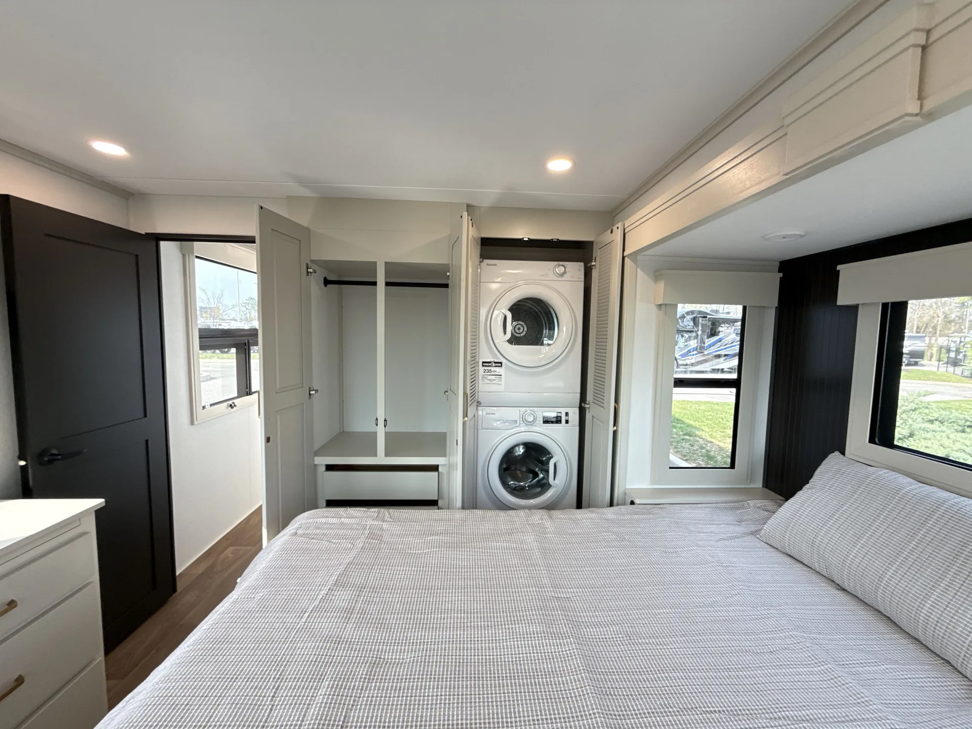 2026 Grand Design Foundation 42GD — Main bedroom with a large bed, open wardrobe, stacked washer and dryer, dresser, and windows