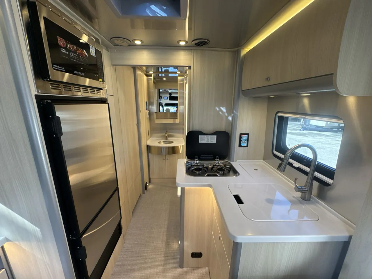 2026 Airstream Atlas Murphy Suite — Class B van kitchen with refrigerator, microwave, two-burner cooktop, sink, faucet, and overhead cabinets