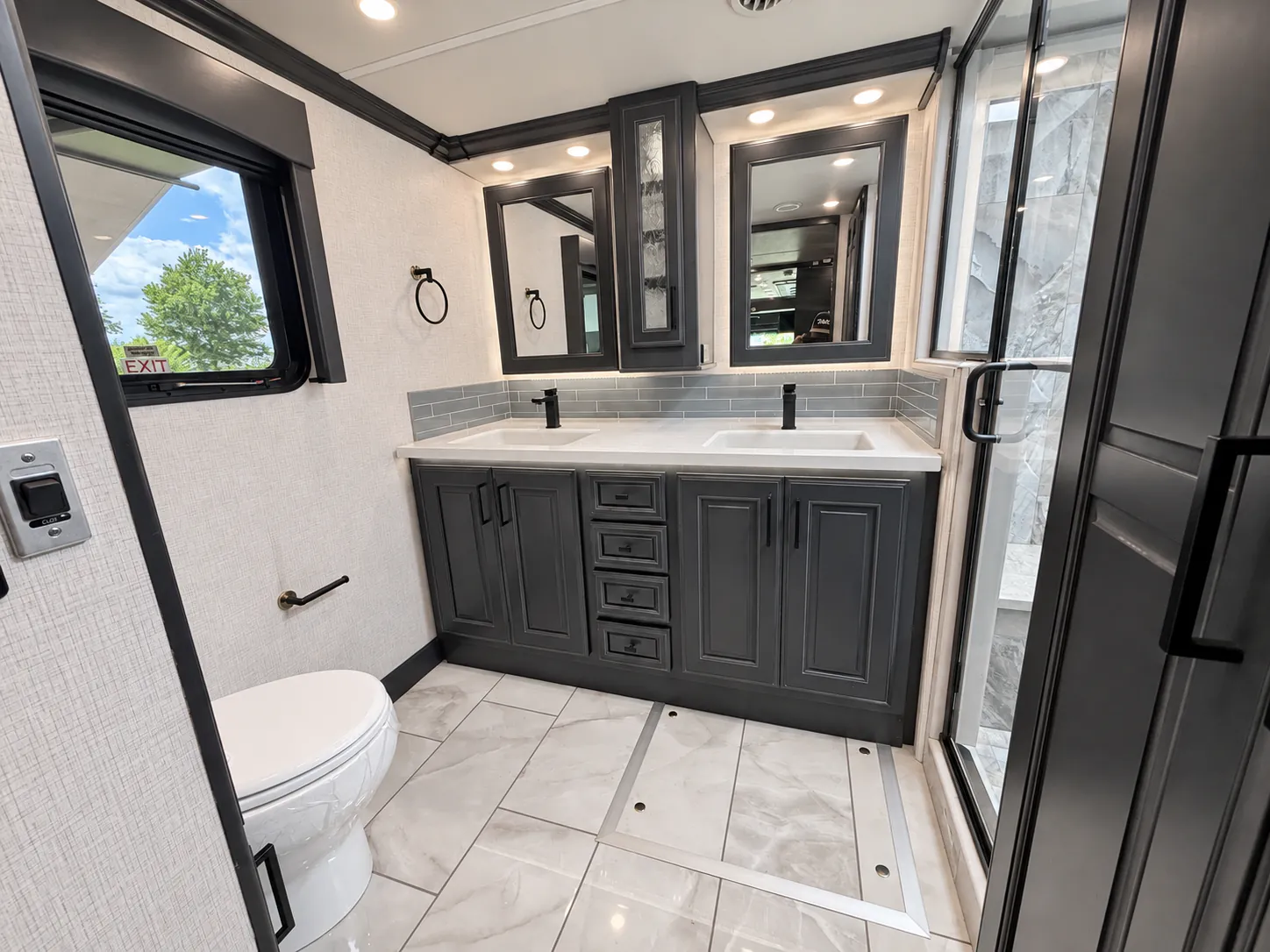 2027 Fleetwood Discovery LXE 40M — Full bathroom with toilet, double-sink vanity, mirrored cabinets, tiled floor, and glass shower
