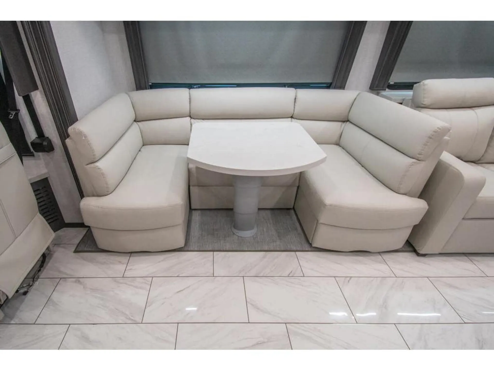 2026 Fleetwood Discovery LXE 40G — U-shaped dinette booth with cream cushions, freestanding pedestal table, windows, and tiled floor