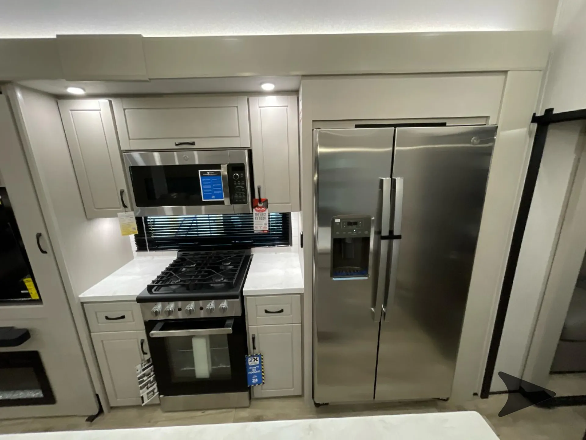 2026 Jayco North Point 377RLBH — Fifth wheel kitchen wall with microwave, gas range, white cabinetry, countertops, and stainless refrigerator