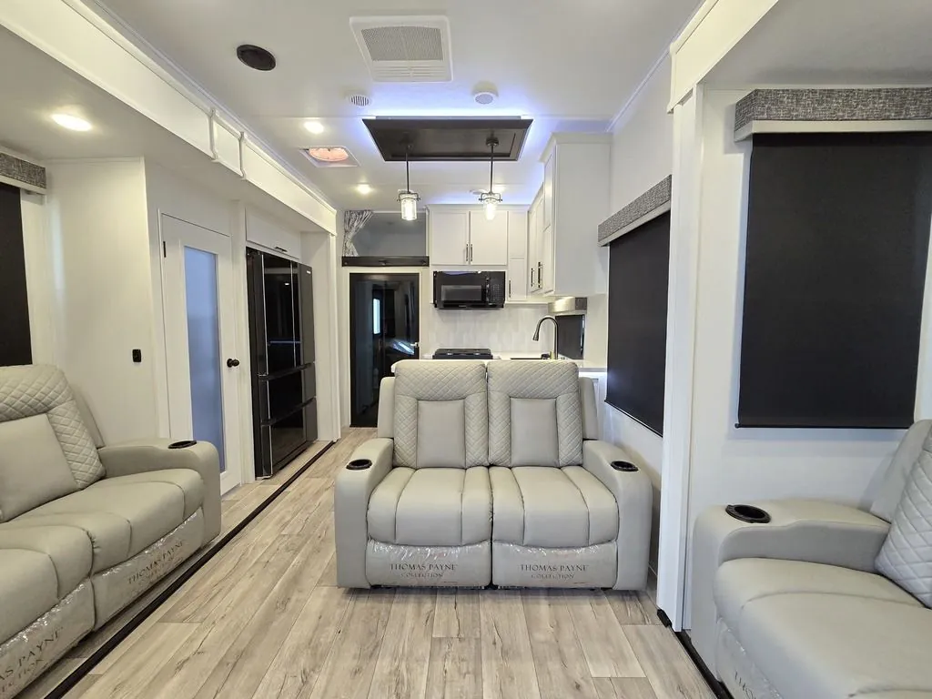 2025 Dutchmen Voltage 4225 — Fifth wheel living room with three recliners facing the entertainment area and kitchen visible behind
