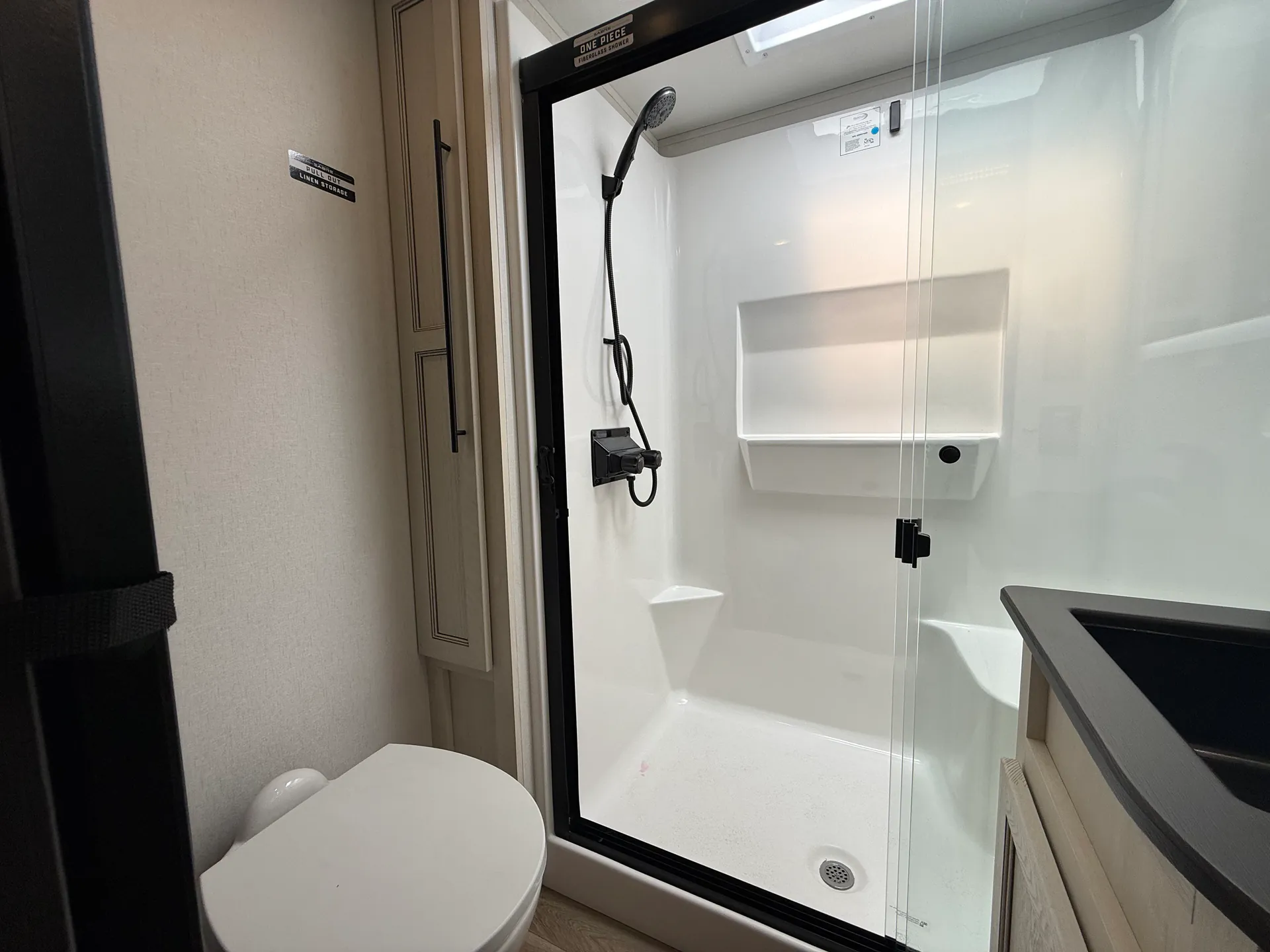 2027 Forest River Sabre 38RVHUNTER — Fifth wheel bathroom showing a glass shower, toilet, vanity edge, and adjacent linen cabinet