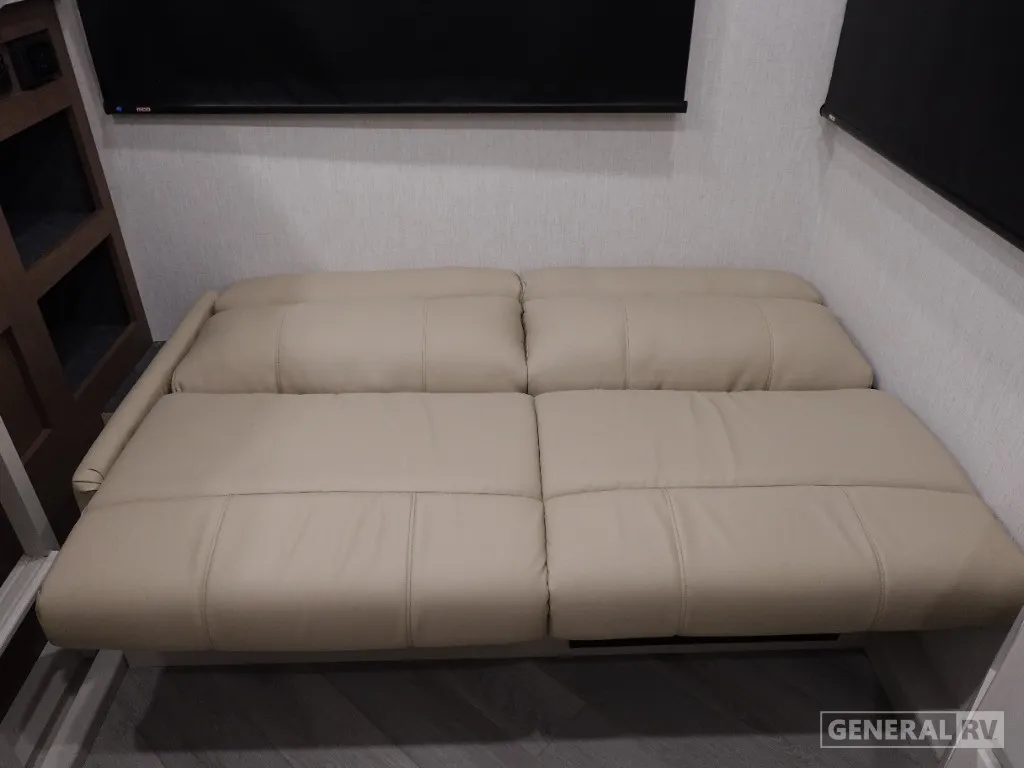 2026 Holiday Rambler Invicta 36Y — Folded leather sofa or lounge seating beneath a wall-mounted television with shelving beside it