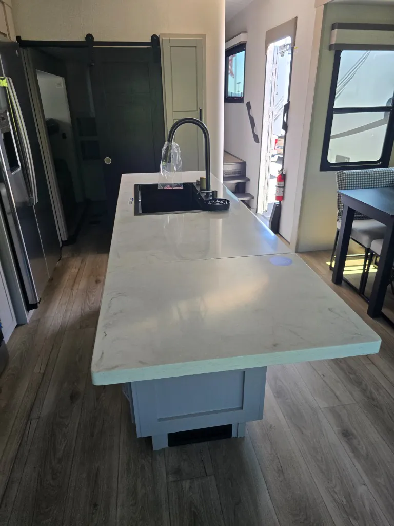 2026 Jayco North Point 377RLBH — Extended kitchen island countertop with sink, refrigerator, barn door, entry steps, and adjacent dining table
