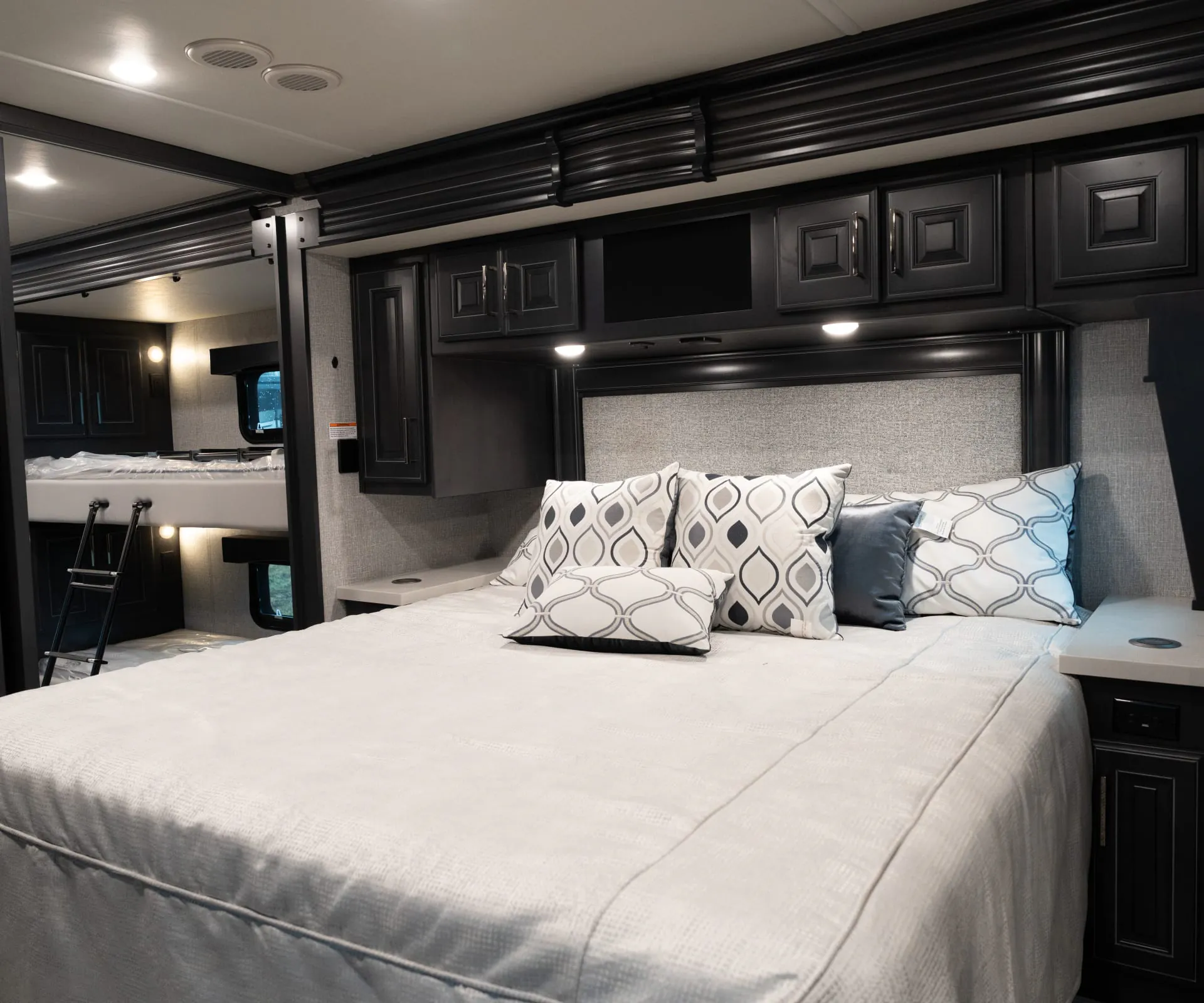2026 Fleetwood Discovery LXE 40G — Main bedroom bed with overhead cabinets and adjacent elevated bunk visible at left