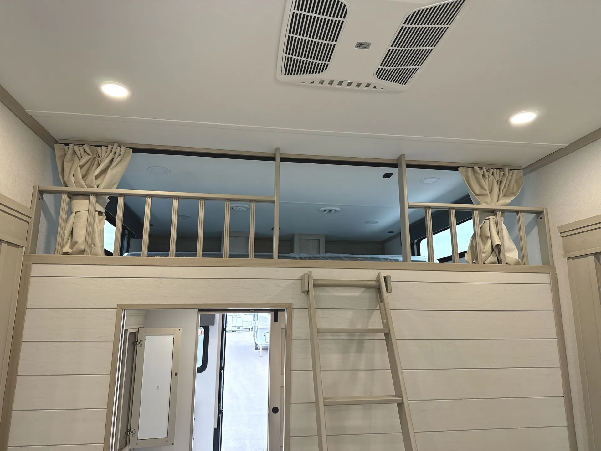 2026 Grand Design Solitude 391DL — Elevated loft sleeping platform with ladder, safety railing, curtains, overhead vents, and access below