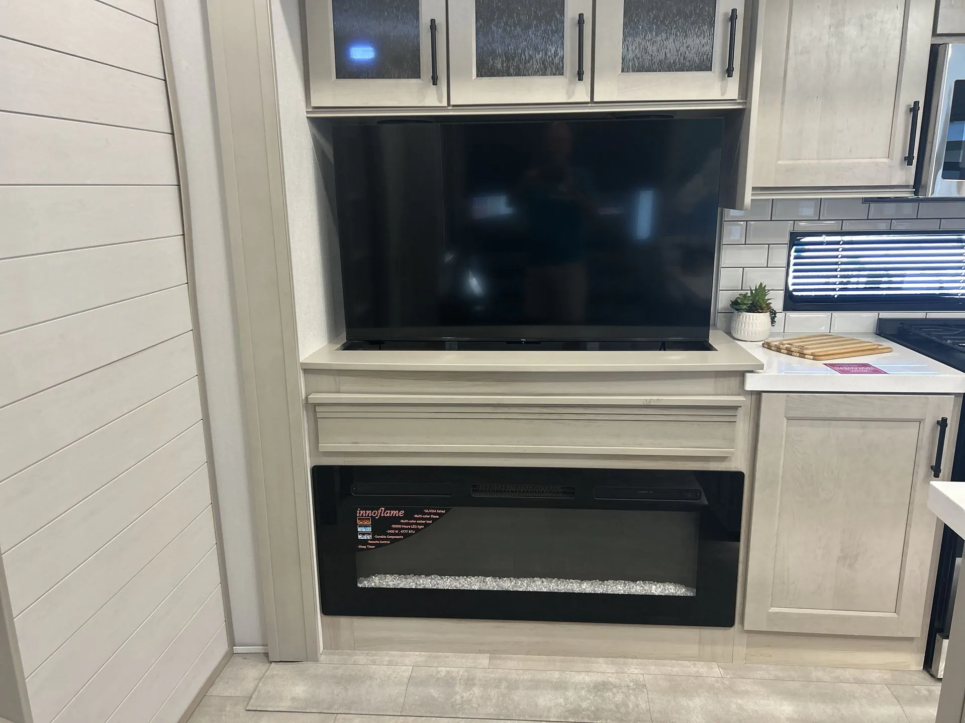 2026 Grand Design Solitude 391DL — Living area entertainment wall with television, cabinetry, electric fireplace, and adjacent kitchen counter