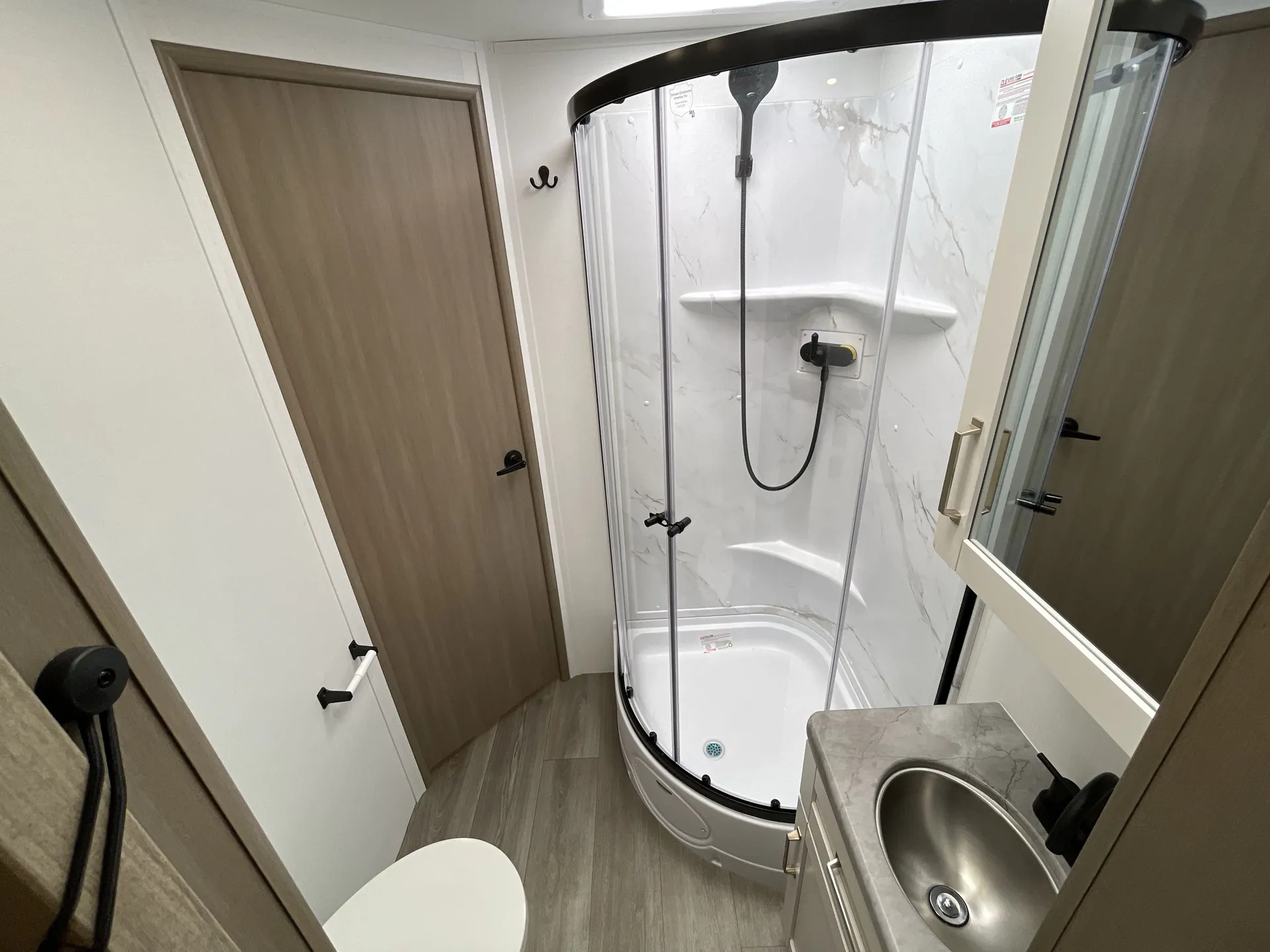 2027 Jayco Alante 29F — Bathroom with a curved glass shower, toilet, vanity sink, wall storage, and wood-look flooring