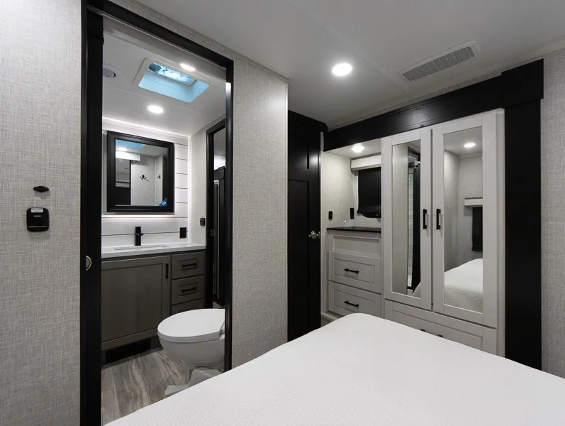 2025 Jayco Seismic Luxury Series 4113 — Bedroom bed and wardrobe beside an open bathroom containing a vanity and toilet