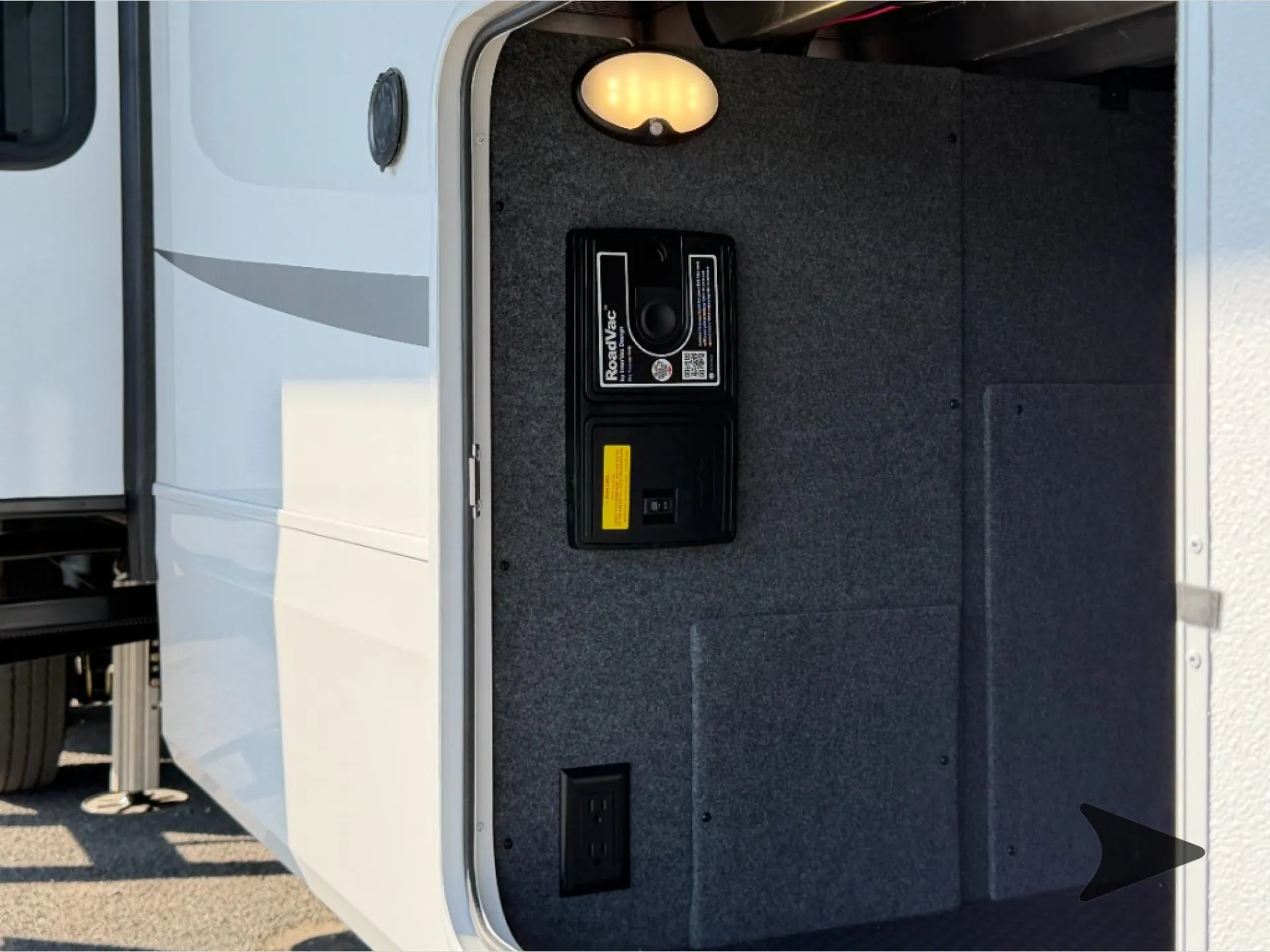 2027 Jayco Pinnacle 39FLOK — Open exterior compartment visibly contains a RoadVac device, electrical outlet, and compartment lighting; this is an exterior-installed utility/service feature