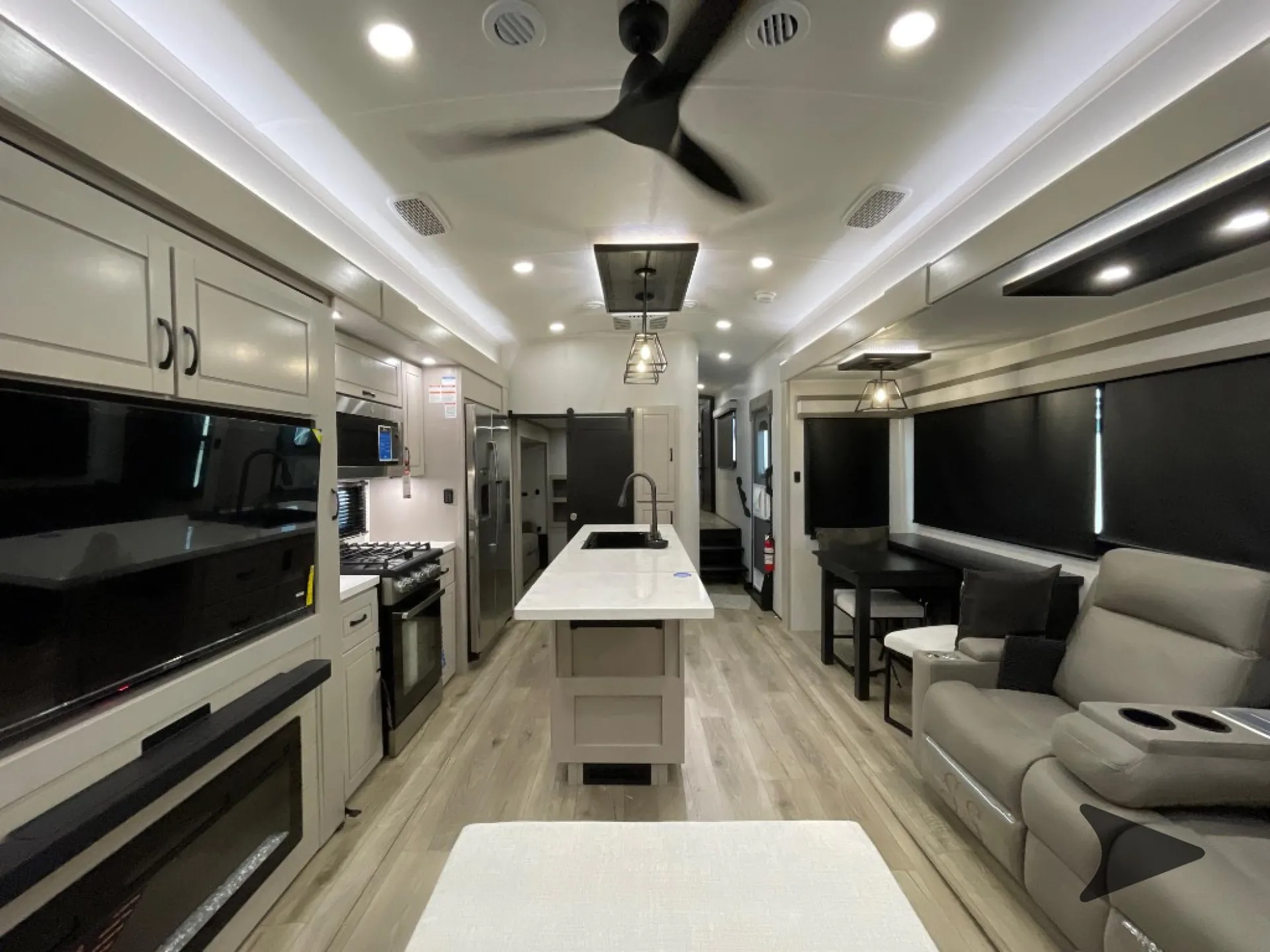 2026 Jayco North Point 377RLBH — Fifth-wheel living area with recliners, sofa, television, dining table, and kitchen island extending toward the rear