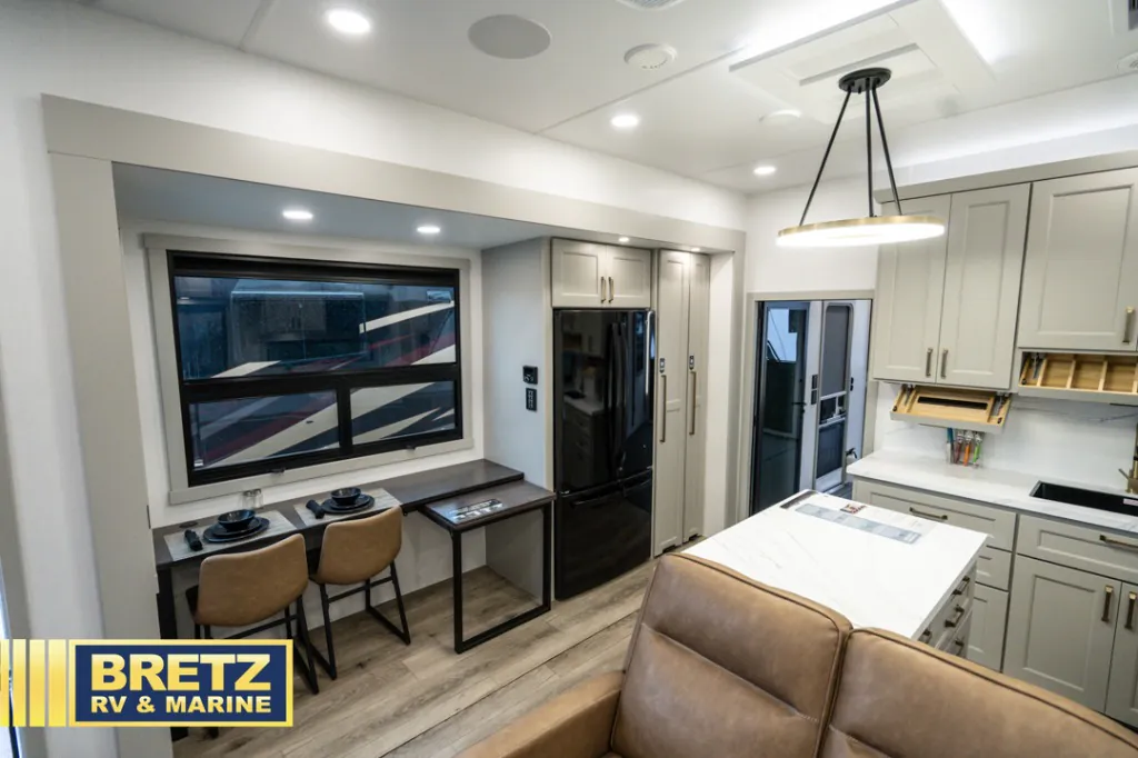 2026 Brinkley Model G 3950 — Fifth wheel interior overview showing a two-seat dining table, refrigerator, kitchen island, cabinetry, and sectional edge