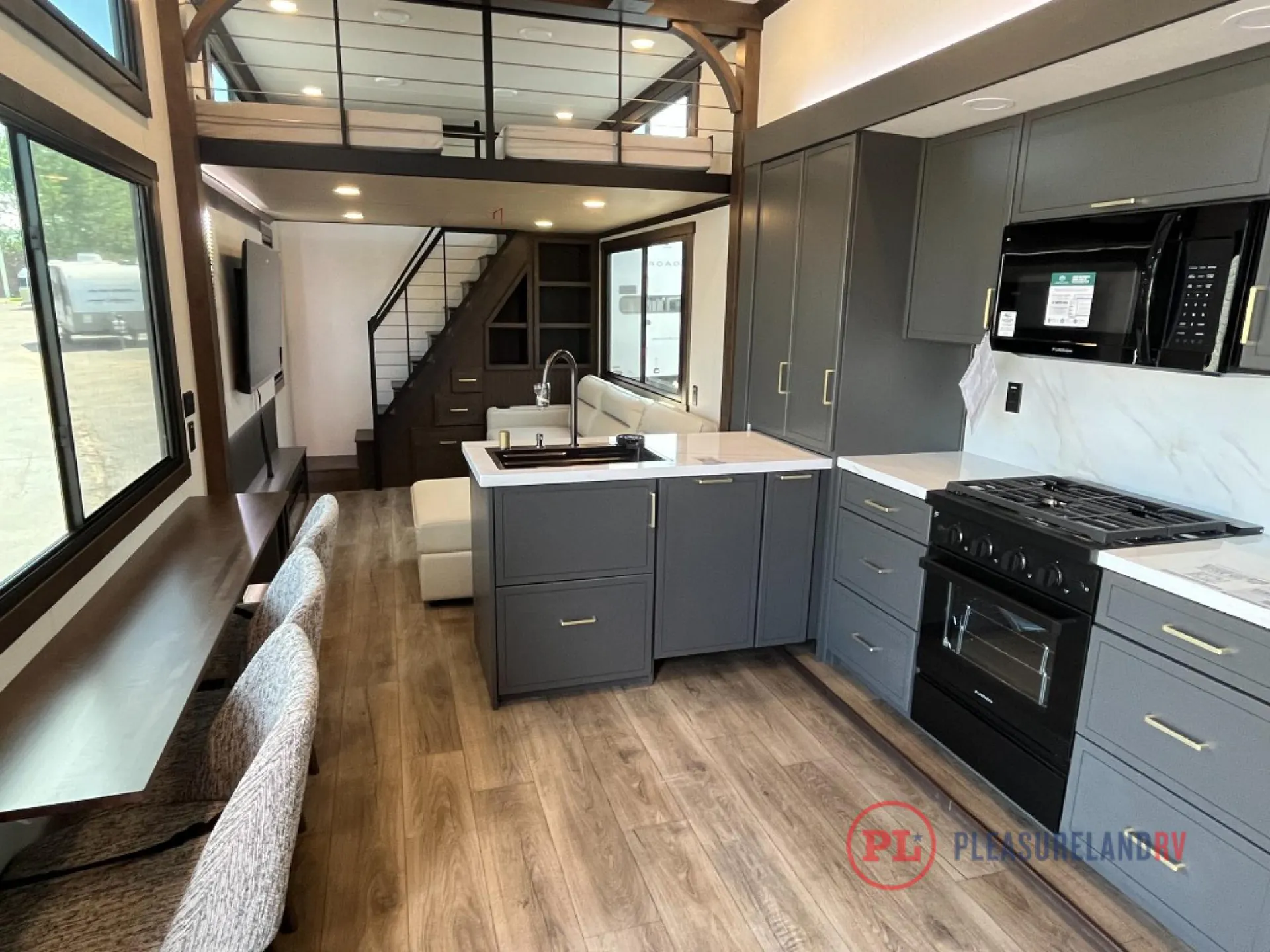 2025 Forest River Cedar Creek Cottage 41FWC — Kitchen cabinetry, sink island, range, dining stools, sofa, stairs, and elevated railing fill a fifth wheel overview