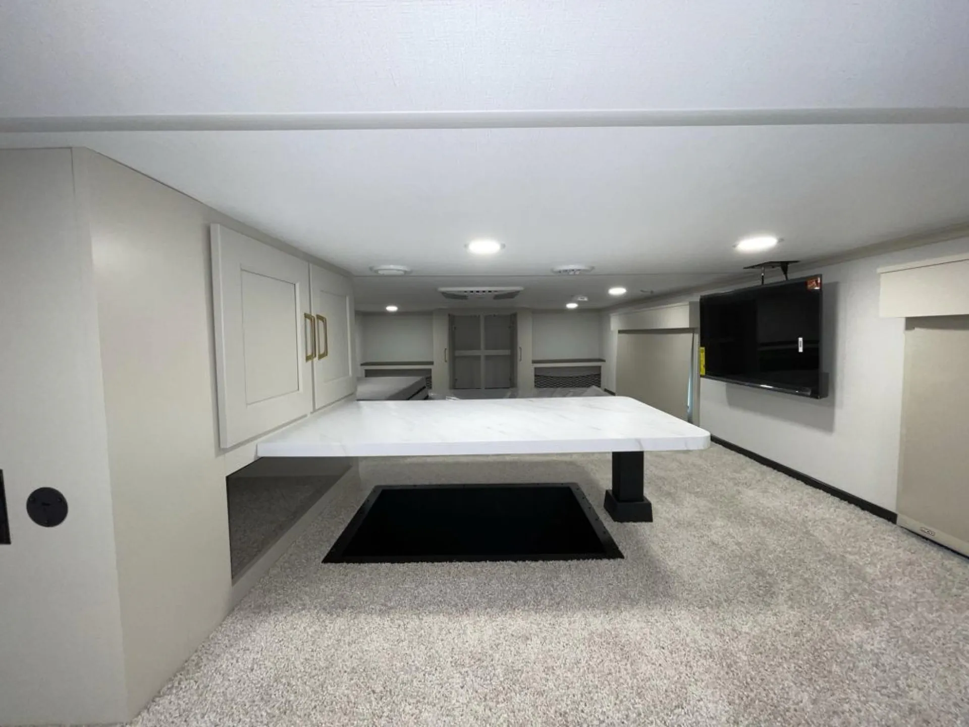 2026 Grand Design Foundation 42GD — Loft overview shows central table, overhead cabinets, wall television, carpeted platforms, and rear sleeping area