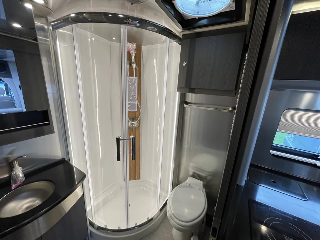 2026 Airstream Atlas Murphy Suite — Class B bathroom with curved shower, toilet, vanity sink, mirrored cabinet, and roof vent