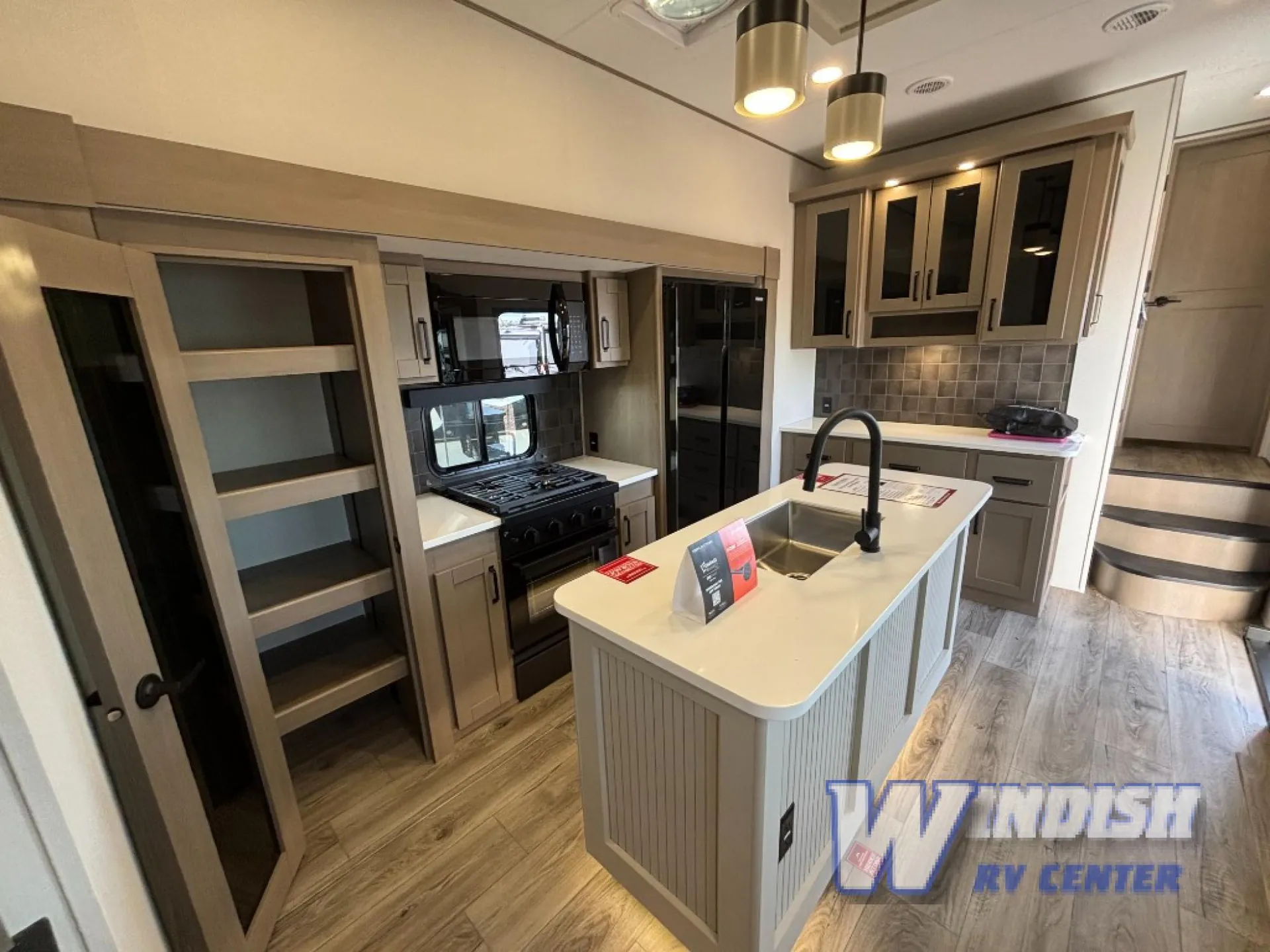 2027 Grand Design Reflection 362TBS — Fifth-wheel kitchen with island sink, gas range, refrigerator, pantry shelves, and backsplash cabinetry
