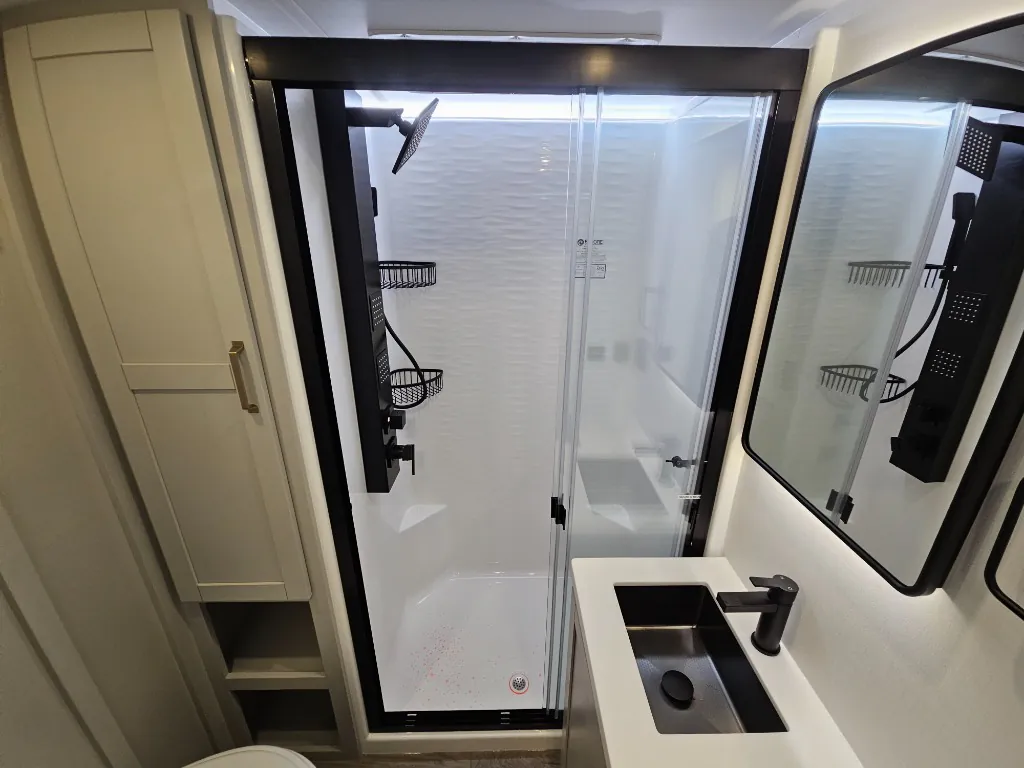 2026 Brinkley Model Z 3515 — Fifth wheel bathroom with glass shower, black shower fixtures, vanity sink, mirror, and adjacent storage cabinet