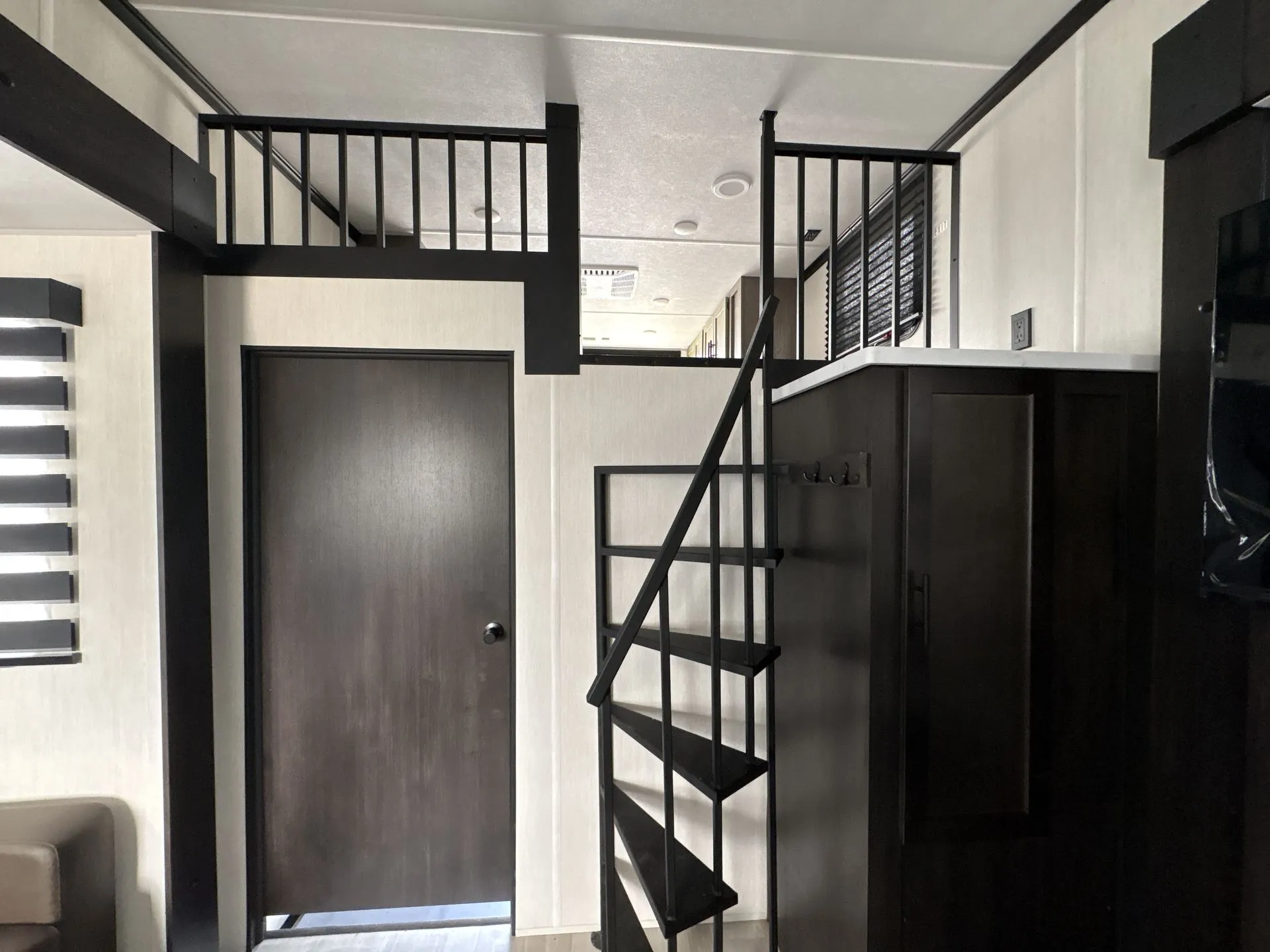 2026 Forest River Cherokee Wolf Pack 397STAY — Staircase leads to an elevated sleeping loft beside dark cabinetry, railings, and an interior door