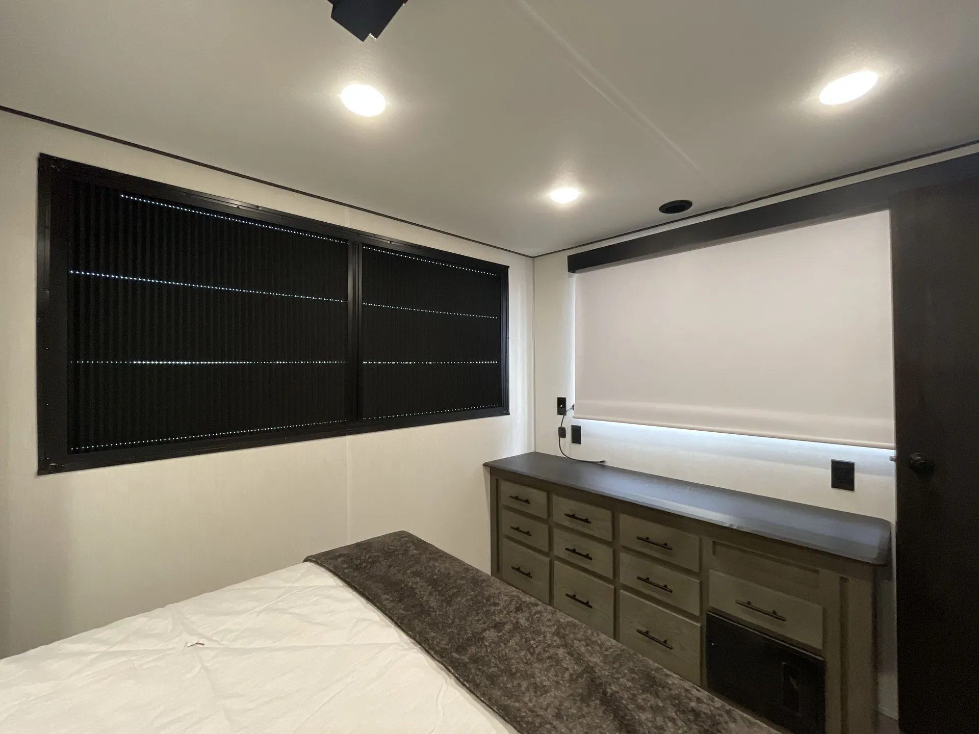 2026 Forest River Cherokee Wolf Pack 397STAY — Travel trailer bedroom with bed, dresser drawers, mini refrigerator, and covered windows