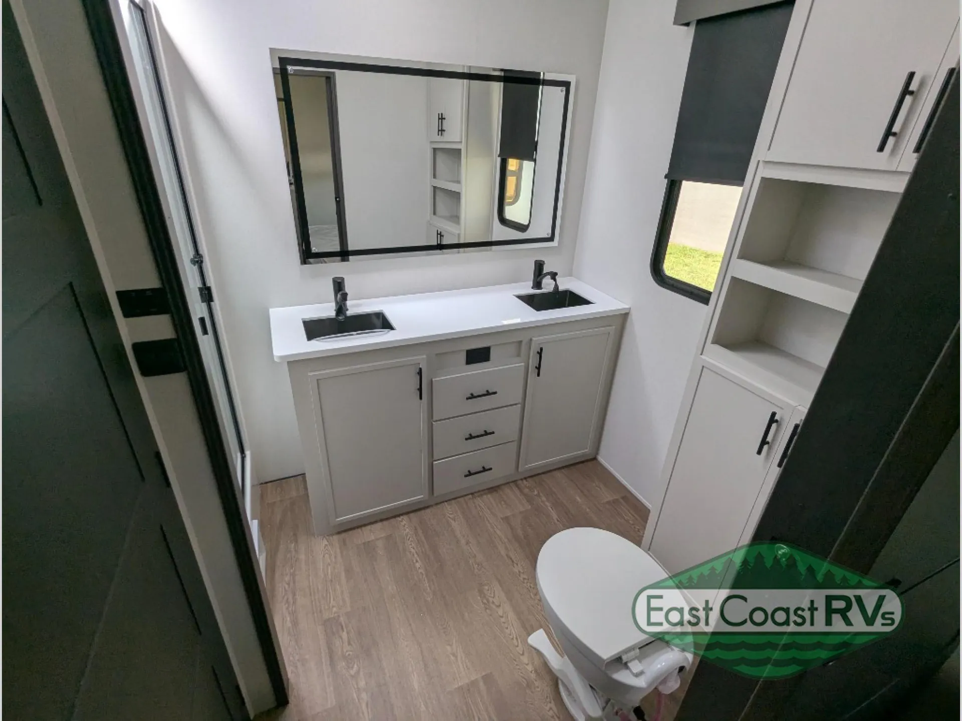 2027 Forest River Sanibel 40BUNK — Fifth wheel bathroom with double-sink vanity, large mirror, toilet, window, and built-in linen shelving