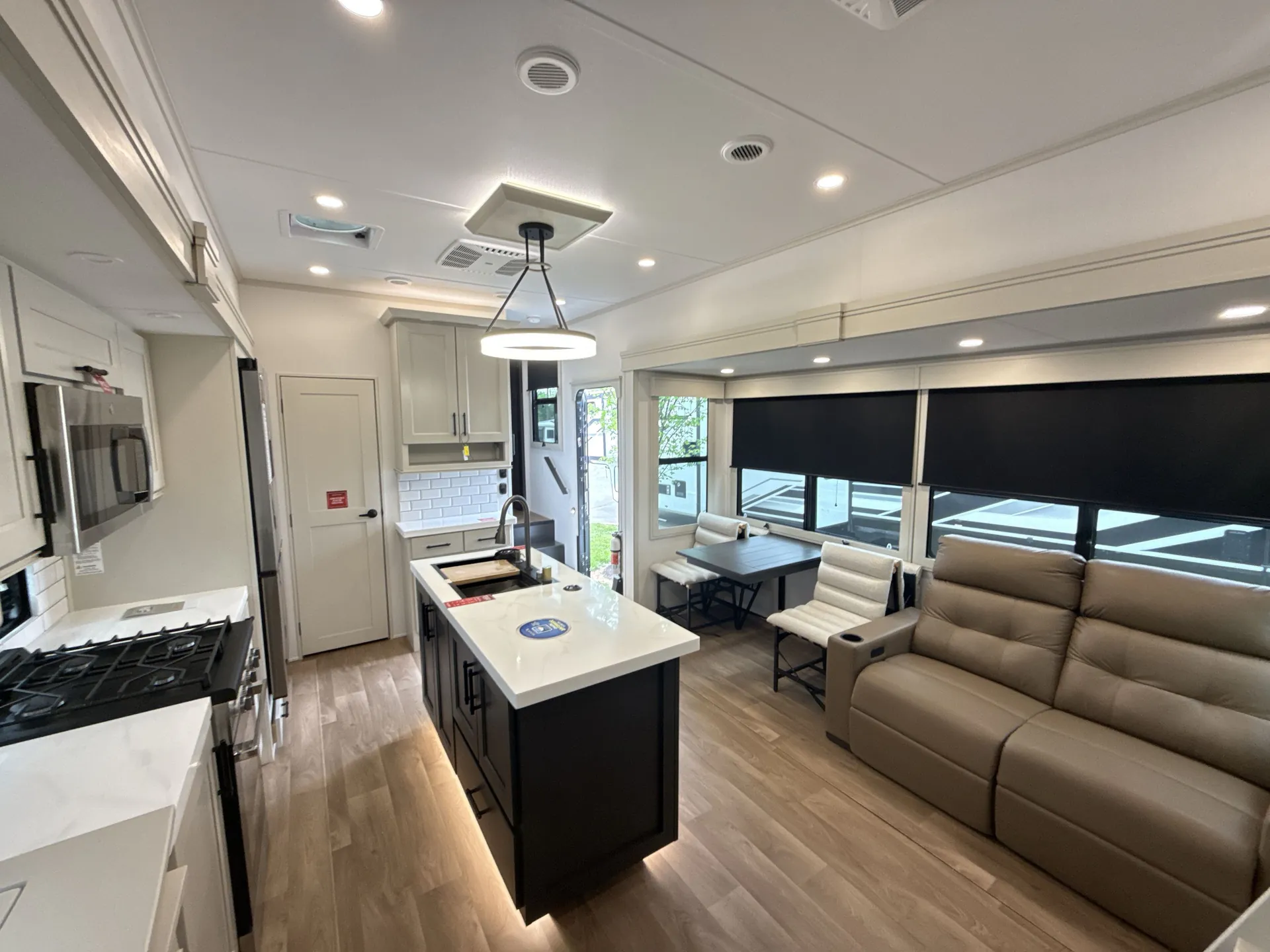 2026 Grand Design Solitude 391DL — Fifth wheel living room with recliner sofa and dining table beside a central kitchen island and appliances
