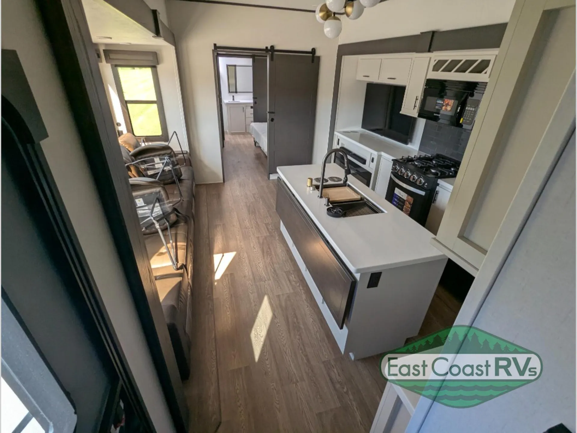 2027 Forest River Sanibel 40BUNK — Fifth wheel interior overview with kitchen island, lounge seating, hallway, bedroom doorway, range, refrigerator, and cabinets