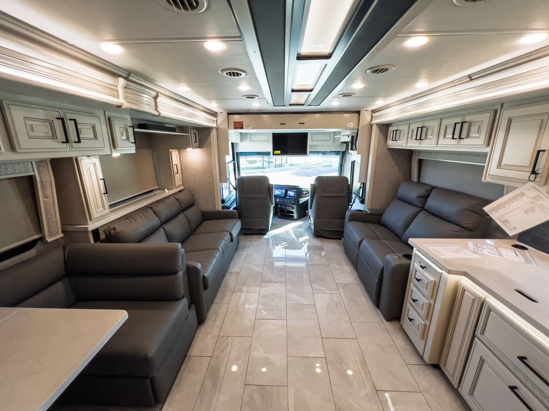 2027 Fleetwood Discovery LXE 40M — Class A interior overview with opposing lounge sofas, front cockpit, entertainment cabinetry, and kitchen counter