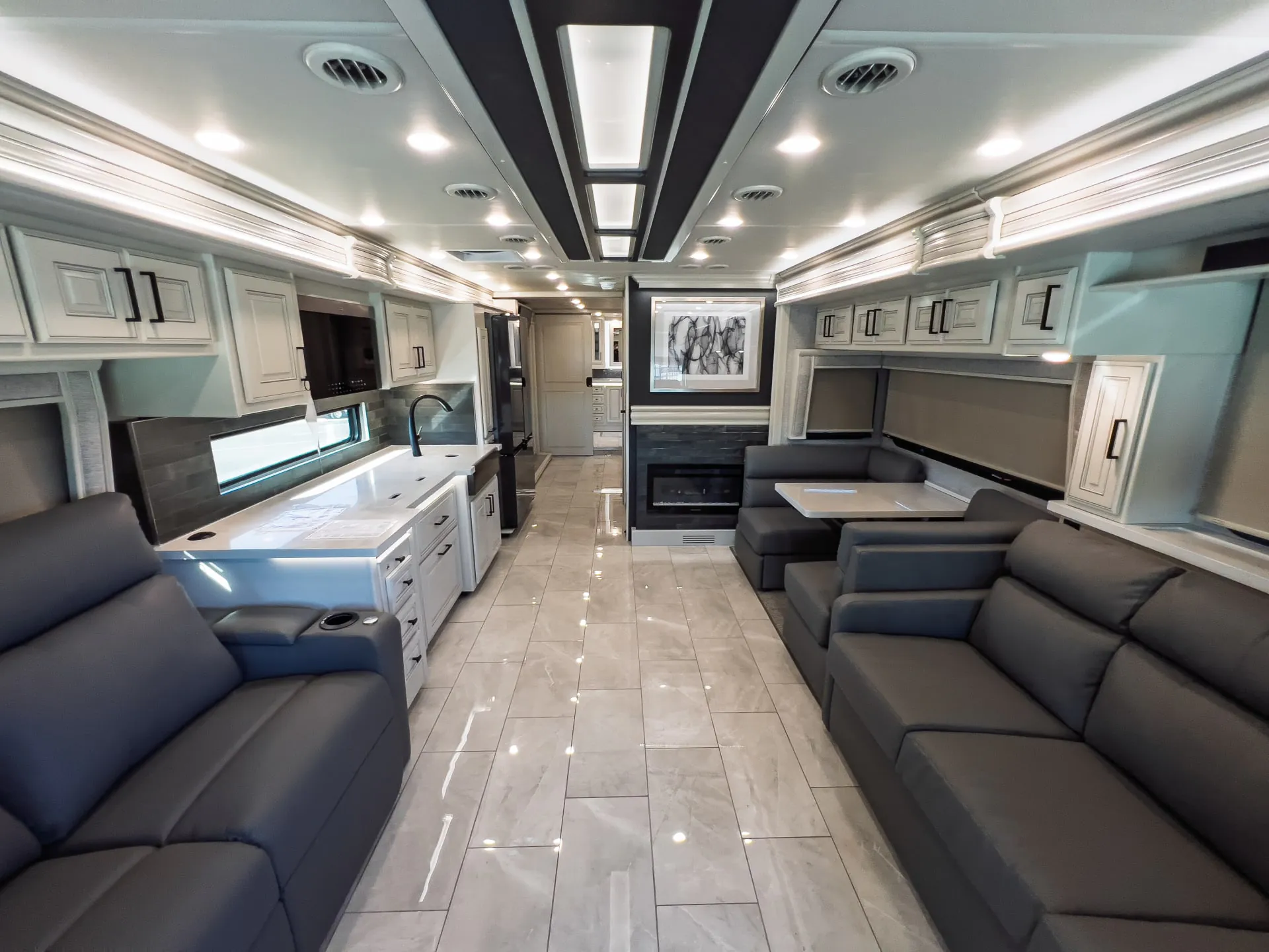 2027 Fleetwood Discovery LXE 40M — Interior overview with opposing sofas, dinette, fireplace, kitchen sink and counter, and hallway cabinetry
