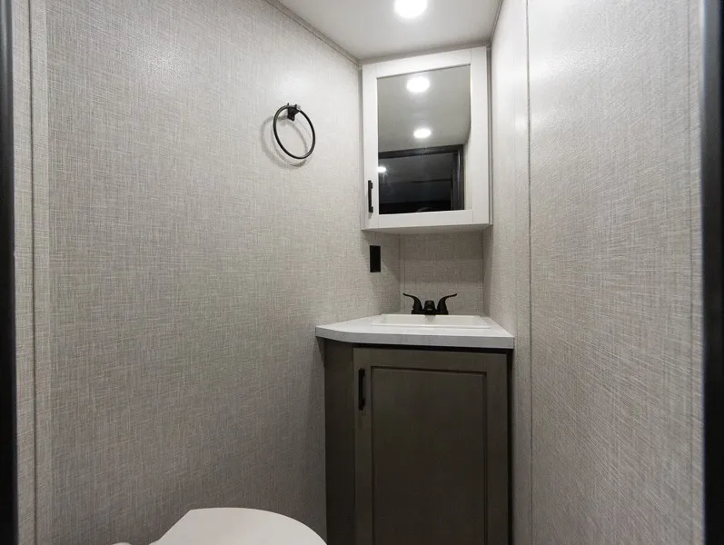2025 Jayco Seismic Luxury Series 4113 — Compact bathroom vanity with sink, faucet, mirrored cabinet, and toilet edge visible at the bottom