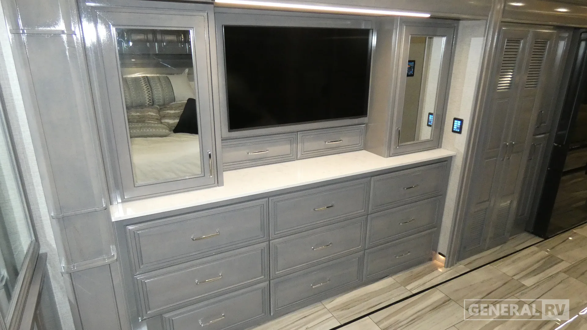 2026 American Coach American Dream 45A — Bedroom entertainment wall with a large television, dresser drawers, mirrored cabinets, and a visible bed reflection
