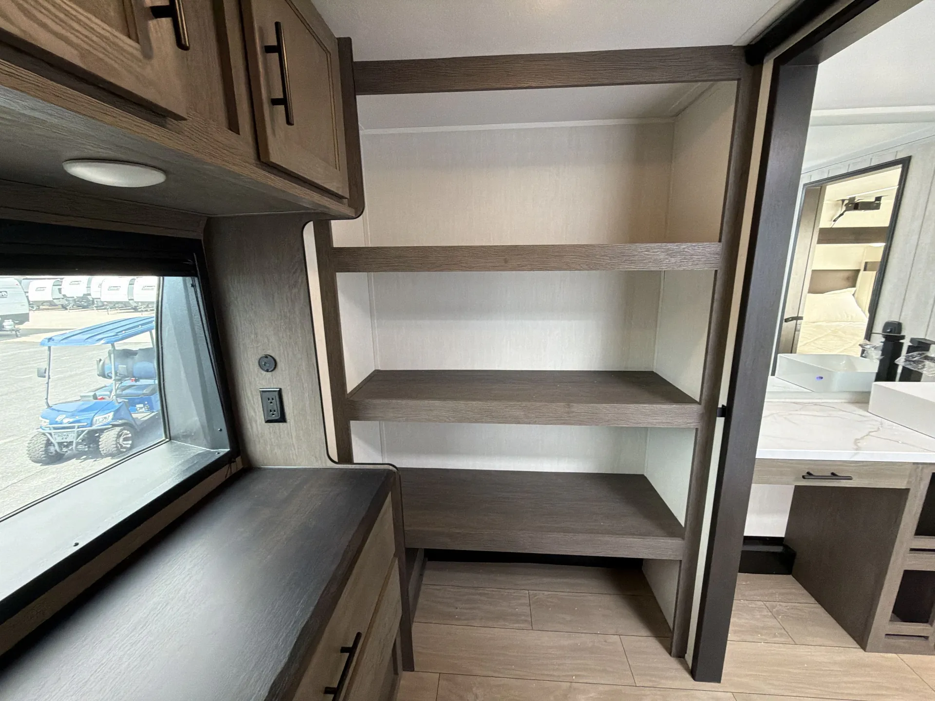 2026 Forest River Arctic Wolf 38LEAH.G — Fifth-wheel bedroom shelving and dresser beside an open doorway revealing a bathroom vanity